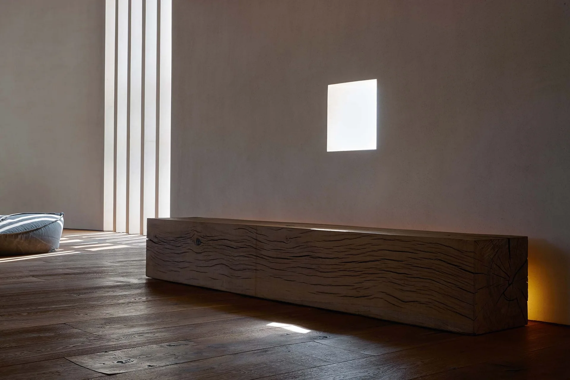 A long raw wood beam bench sits on dark hardwood floors against a matte off-white wall with an integrated square light cutout.