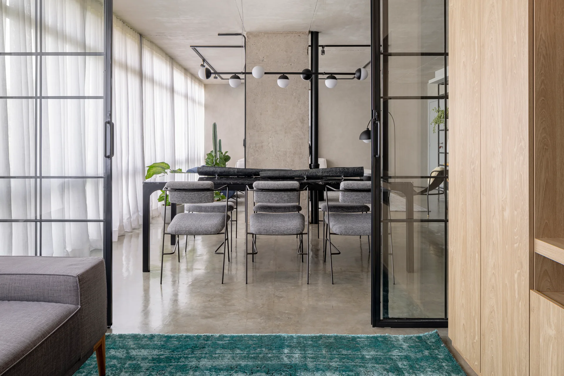 A modern dining room with grey chairs and a black table viewed through black-framed glass sliding doors, featuring a concrete column.