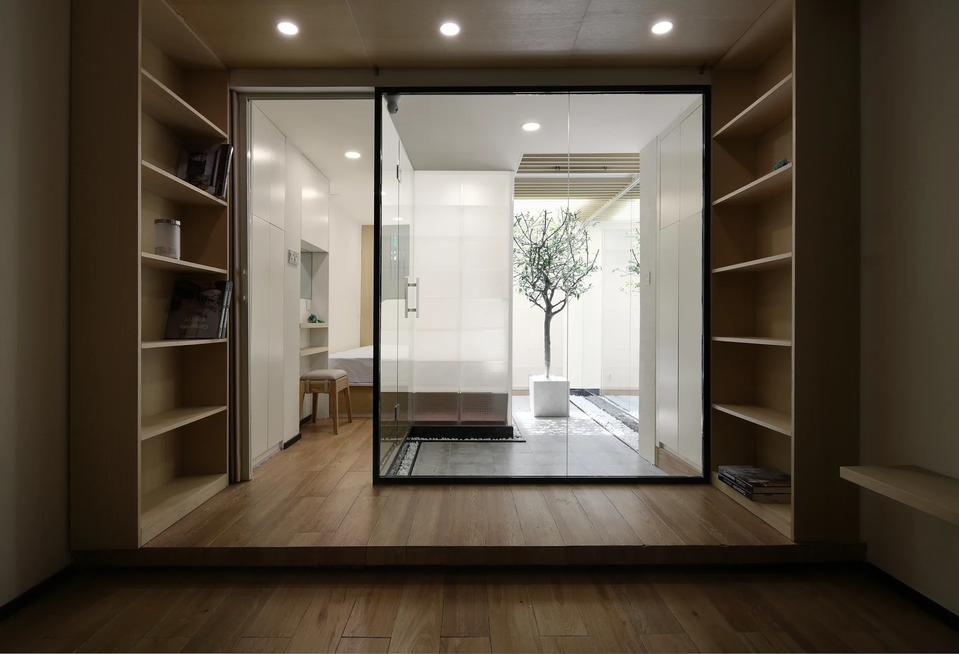 Wooden built-in shelving units flank a central sliding glass door opening onto a minimalist interior courtyard with a potted tree.