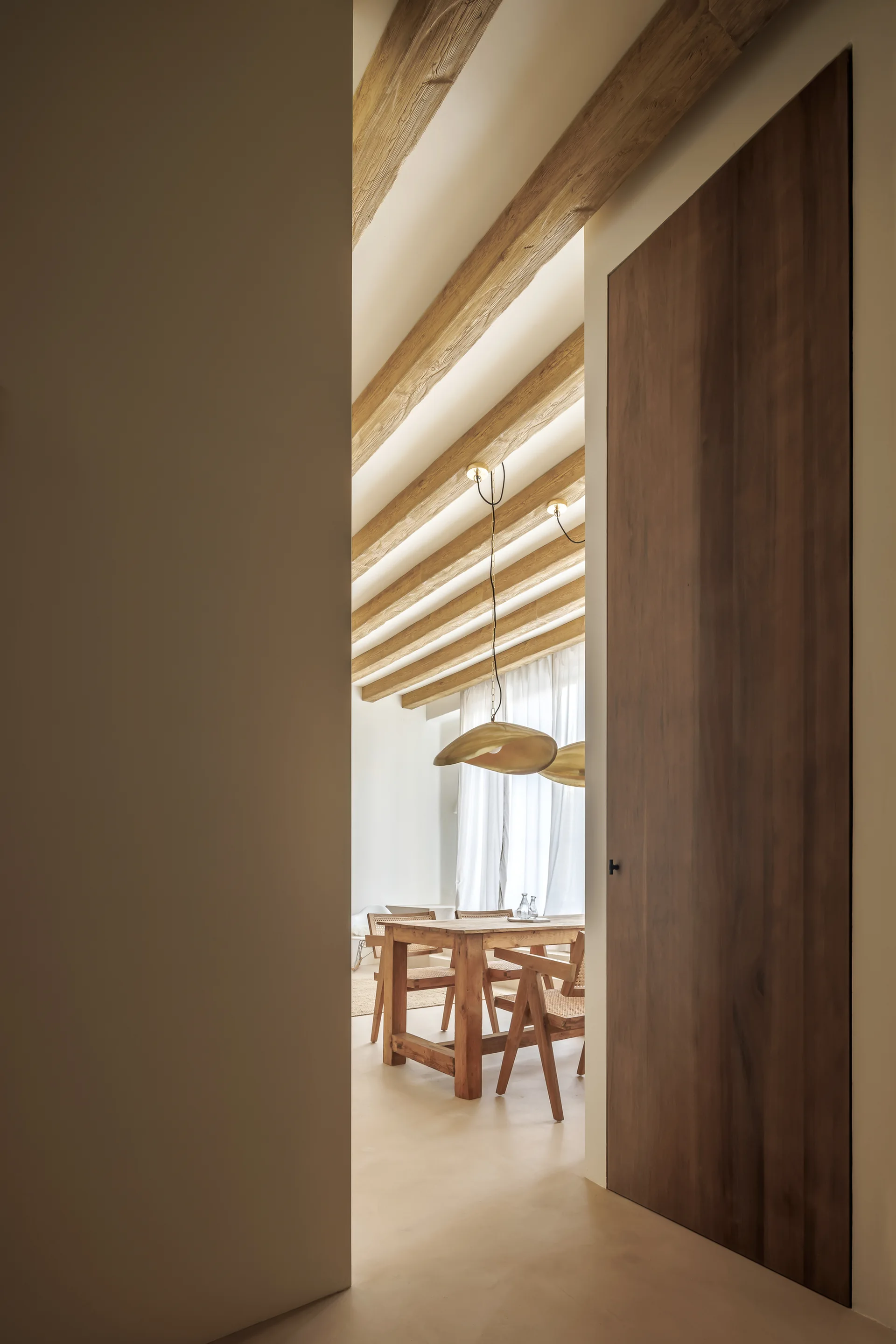 A view through a wooden doorway reveals a dining area with a rustic wooden table, cane-back chairs, and exposed wooden beams on the ceiling.