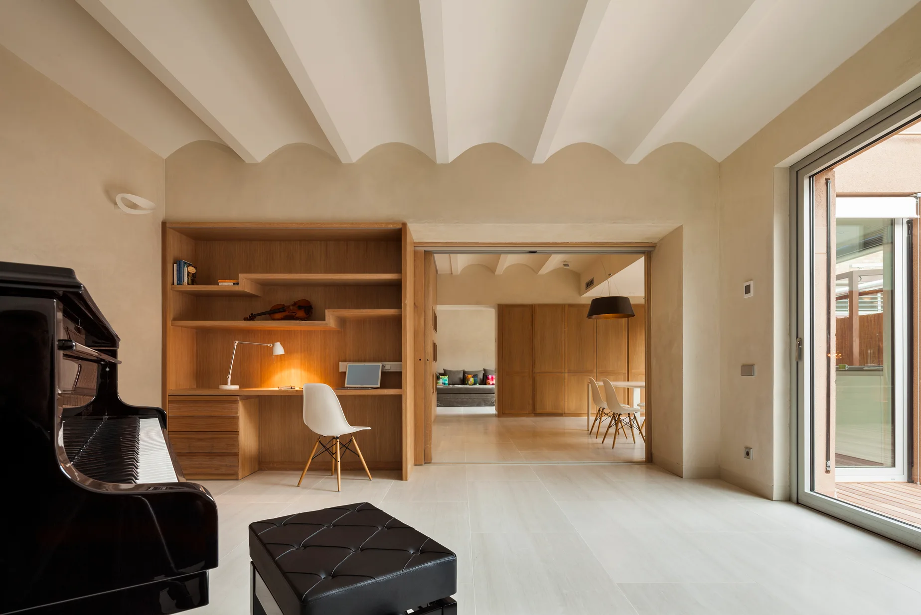 A minimalist living room features a unique scalloped vaulted ceiling, a black grand piano, and a large built-in wooden desk unit.