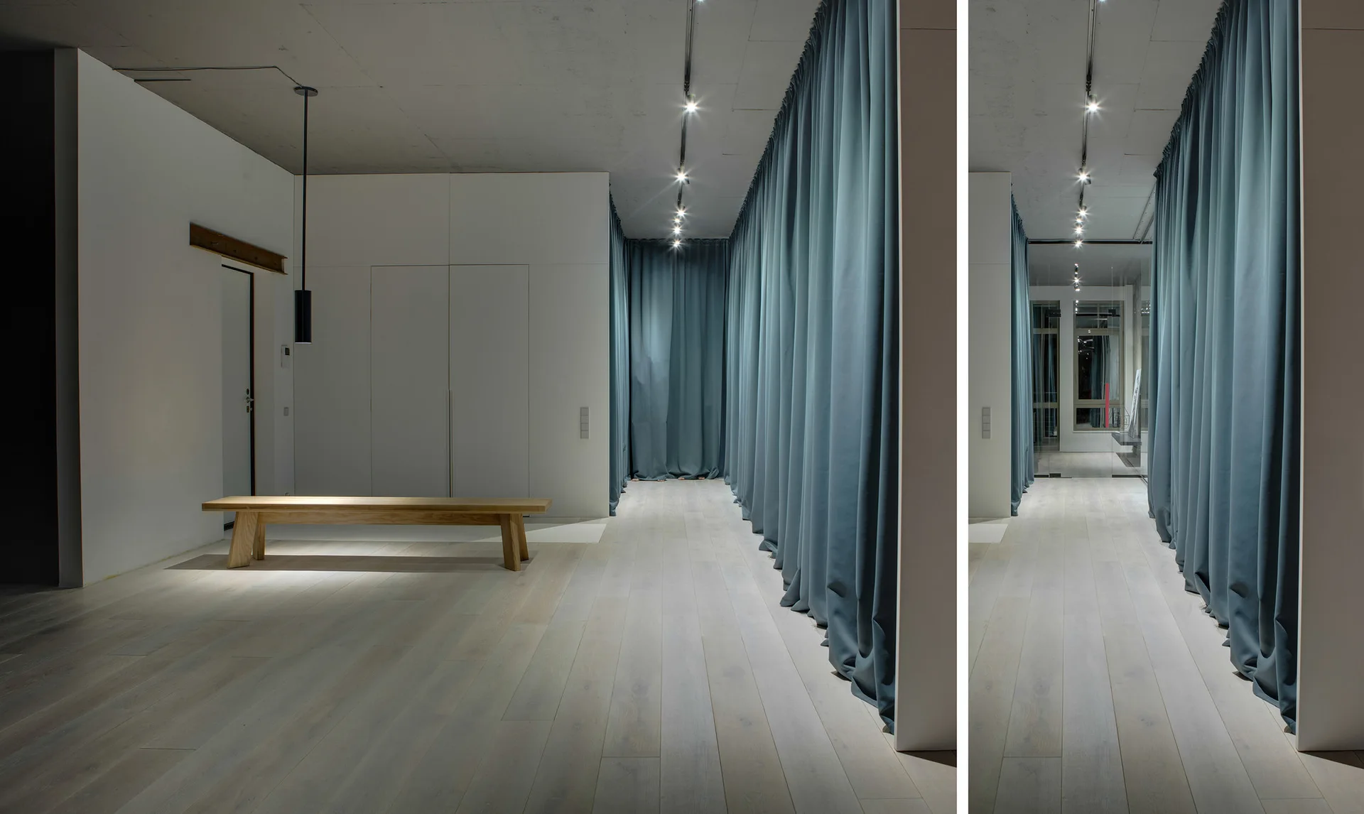 A minimalist hallway featuring a long wall of teal curtains on the right, a low wooden bench, and a modern pendant light on the left.