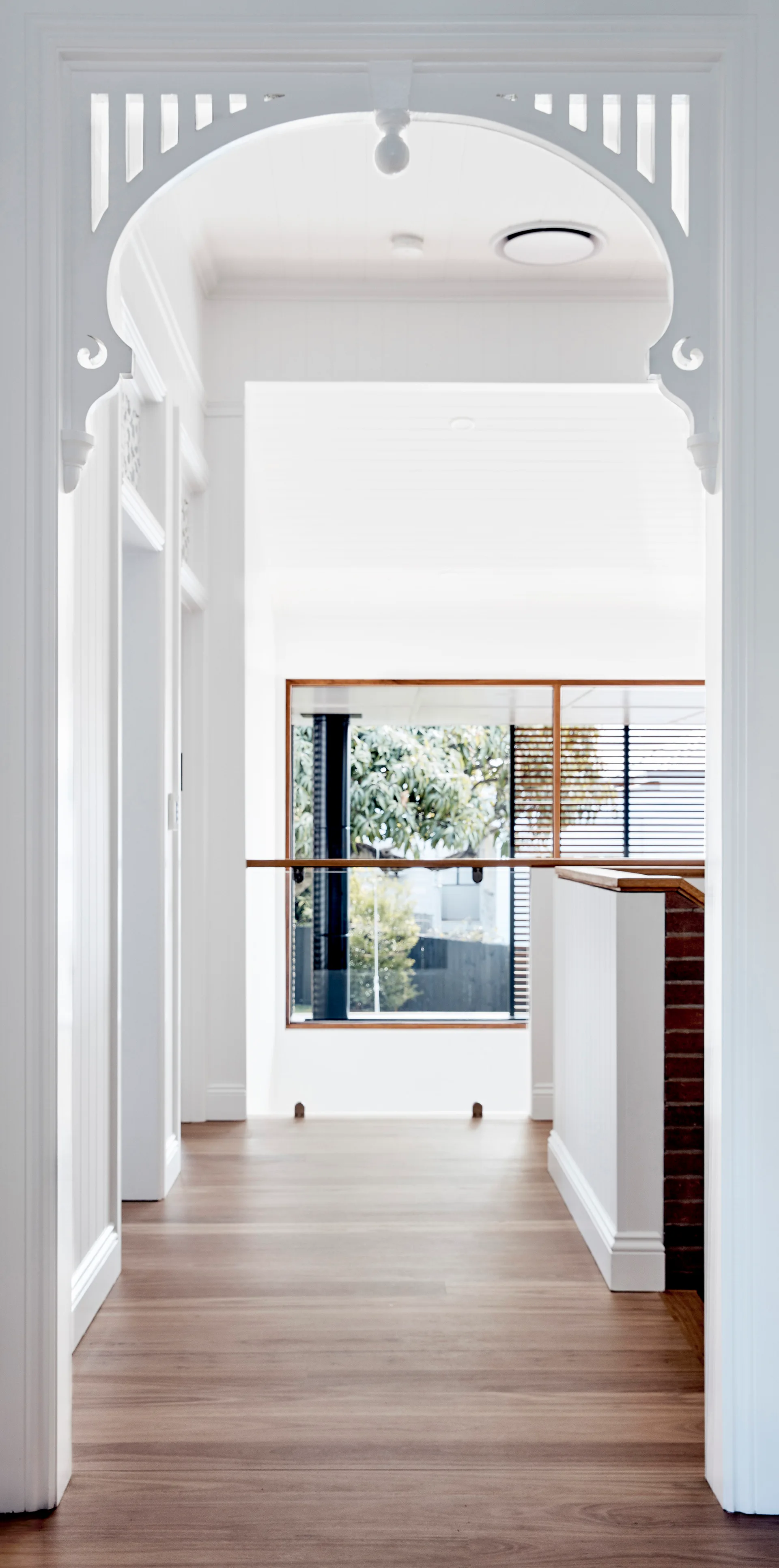 A bright white residential hallway featuring medium-toned wood floors, vertical wainscoting, and a decorative white fretwork archway framing the entry.