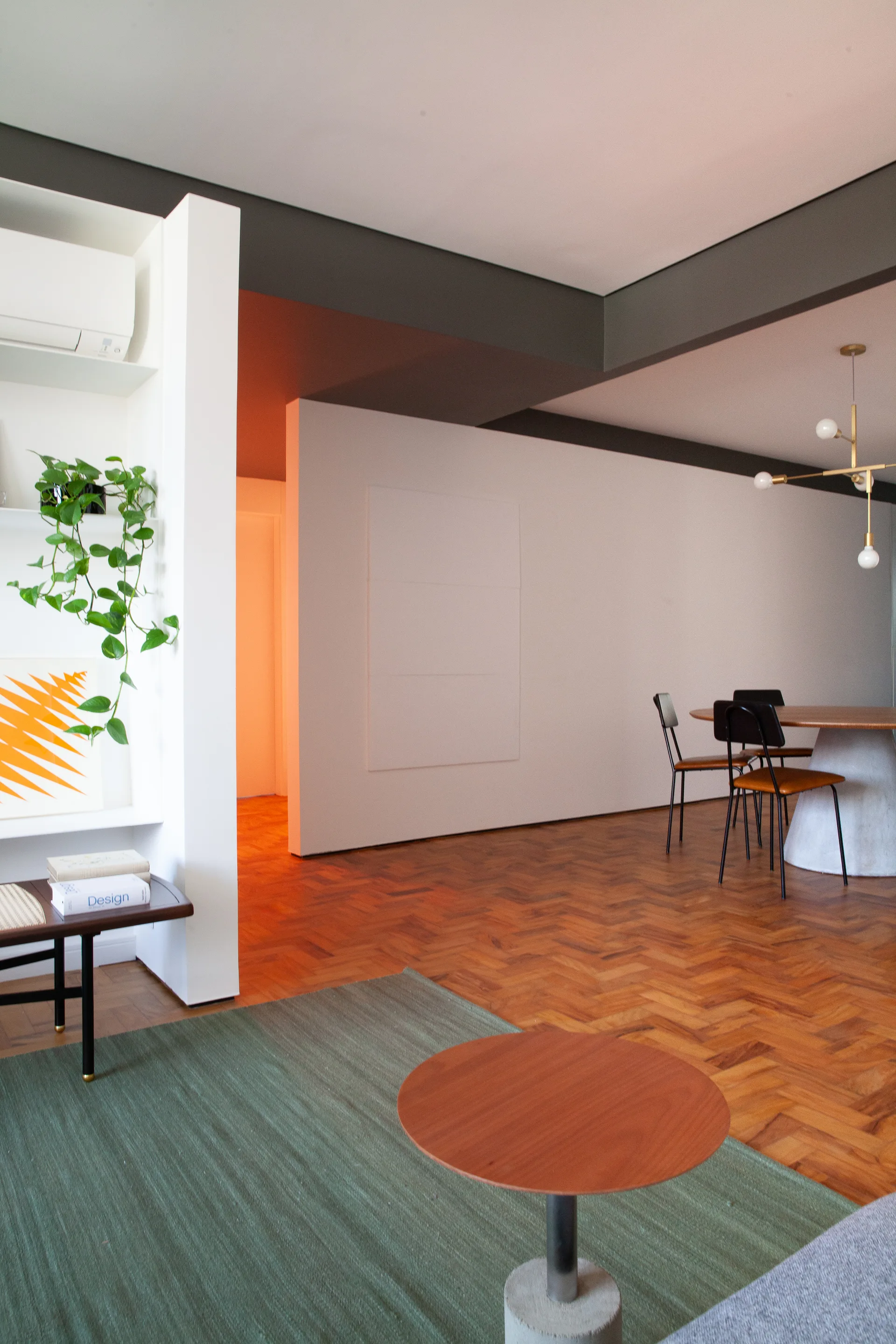 A modern dining room featuring parquet herringbone floors, a white partition wall, a circular wooden dining table, and built-in shelving with plants.