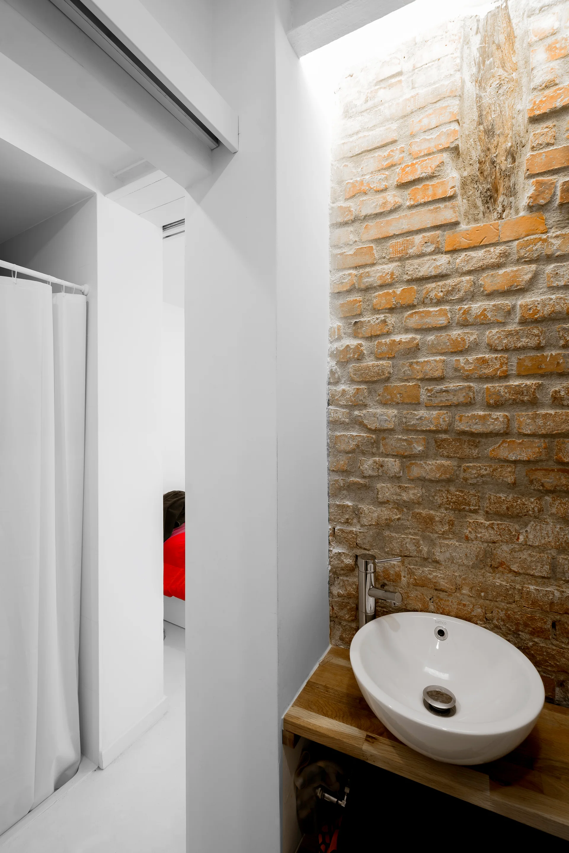 A bathroom vanity features a white ceramic vessel sink on a wooden countertop against a textured exposed brick wall.