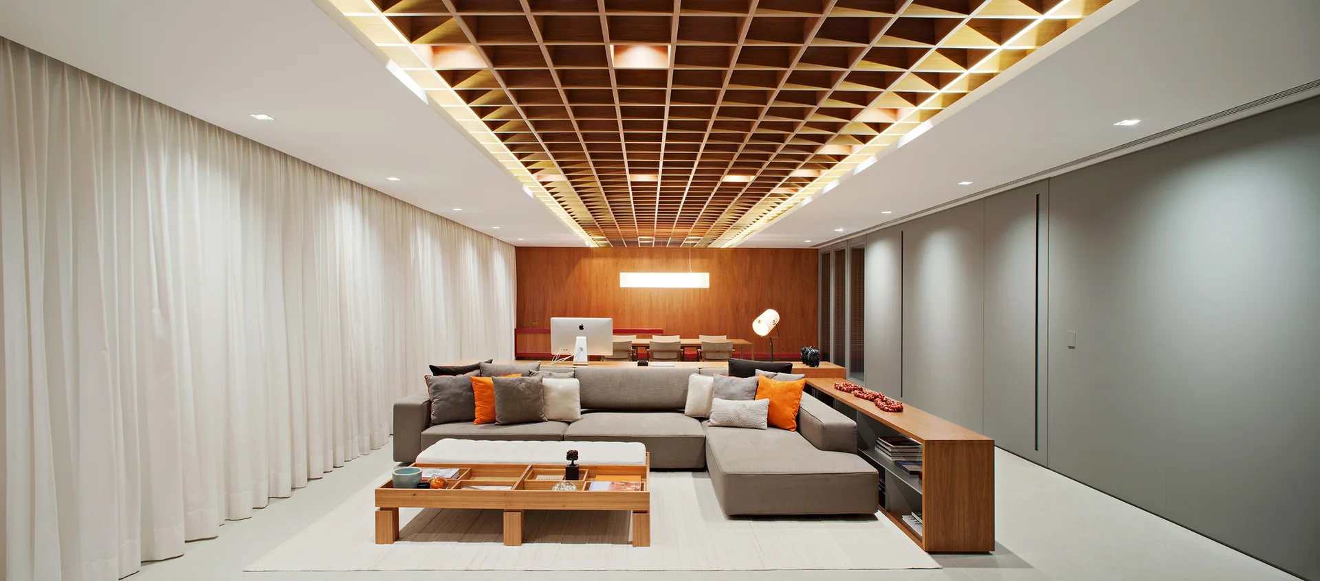 A modern living room features a grey sectional sofa, a wooden grid ceiling with recessed lighting, and a matching wood-paneled accent wall.