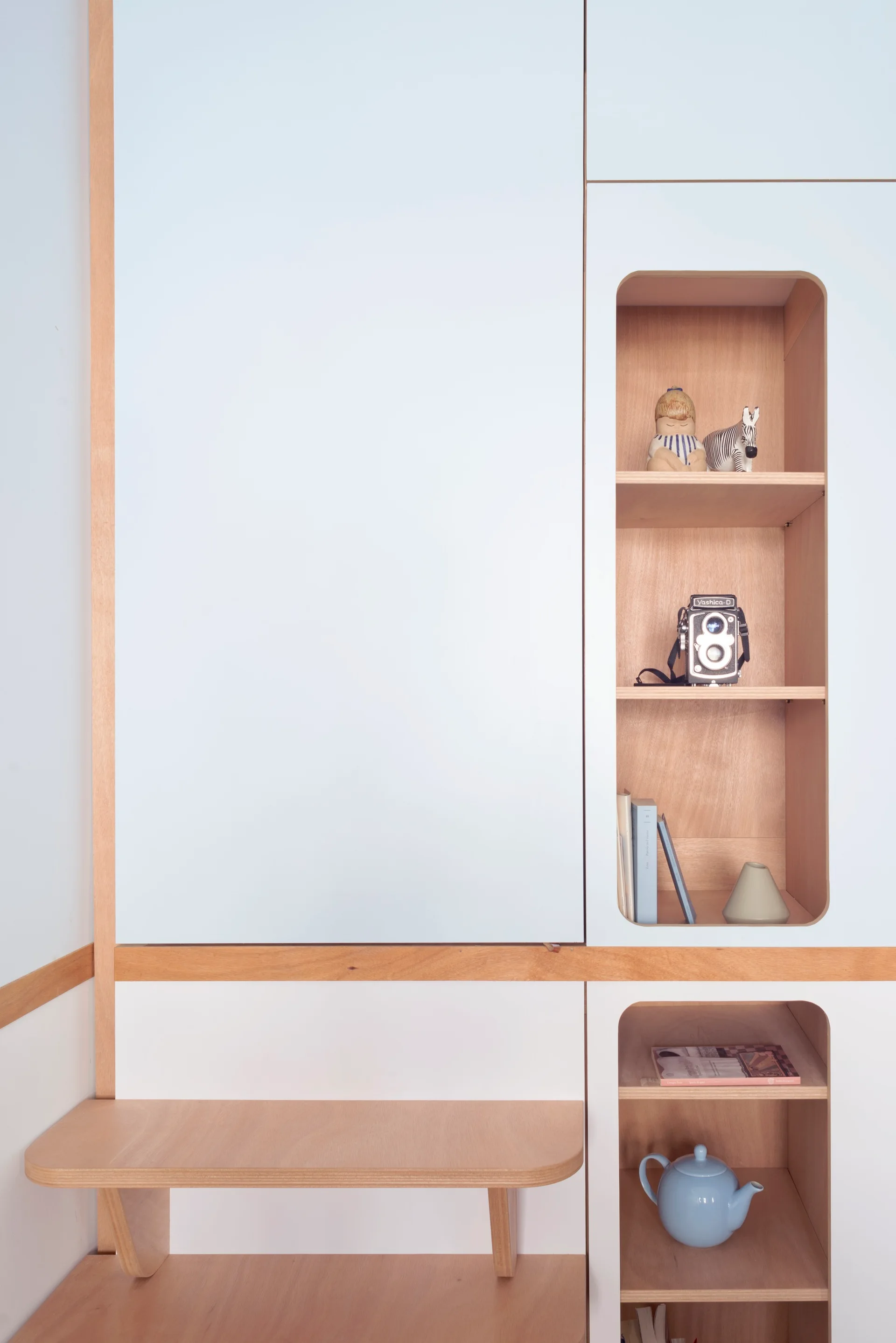 A minimalist built-in cabinet unit with light blue panels, natural wood lining, and rounded alcoves displaying decorative objects.