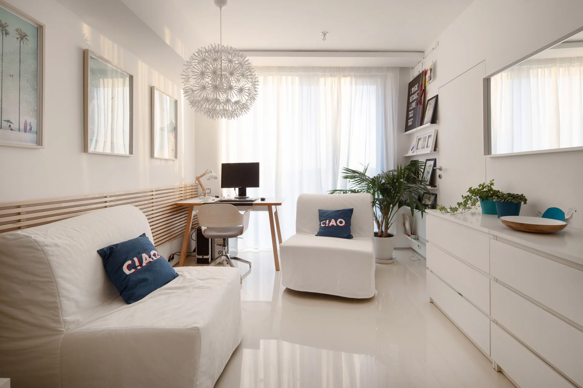 A bright Scandinavian living room featuring white sofas, a glossy white floor, a light wood desk, and a distinctive spiky white pendant light.