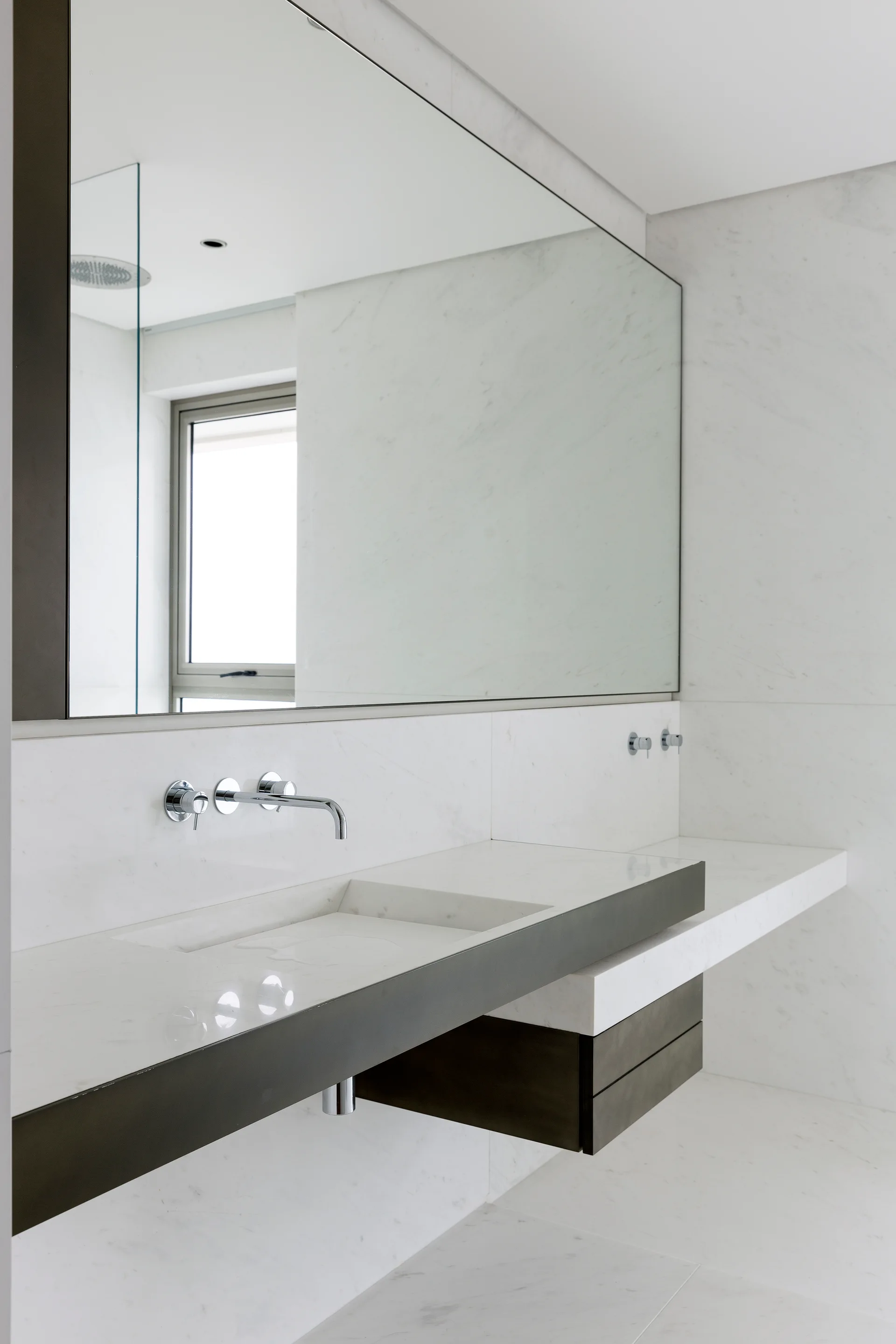 A modern bathroom features a floating white marble vanity with an integrated sink, a chrome wall-mounted faucet, and a large rectangular mirror.