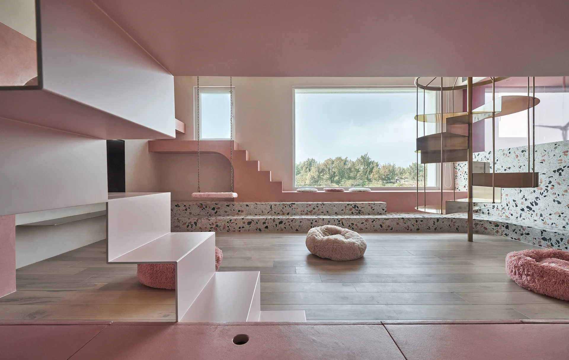A minimalist pink room features a terrazzo-clad stepped platform, a metallic spiral staircase, and a geometric pink staircase over light wood floors.