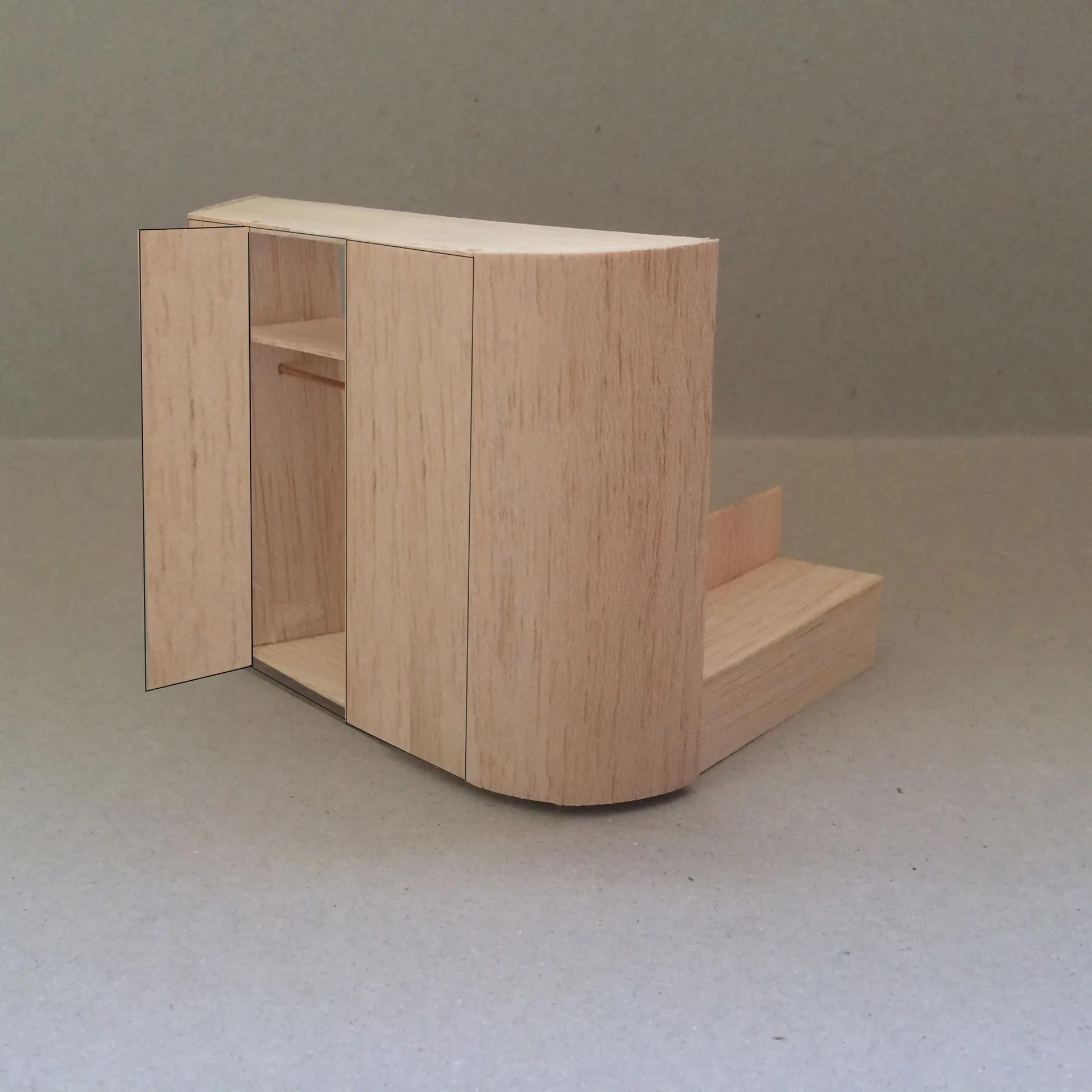 A small balsa wood architectural model of a wardrobe cabinet with a curved edge, open door, and adjacent stairs.