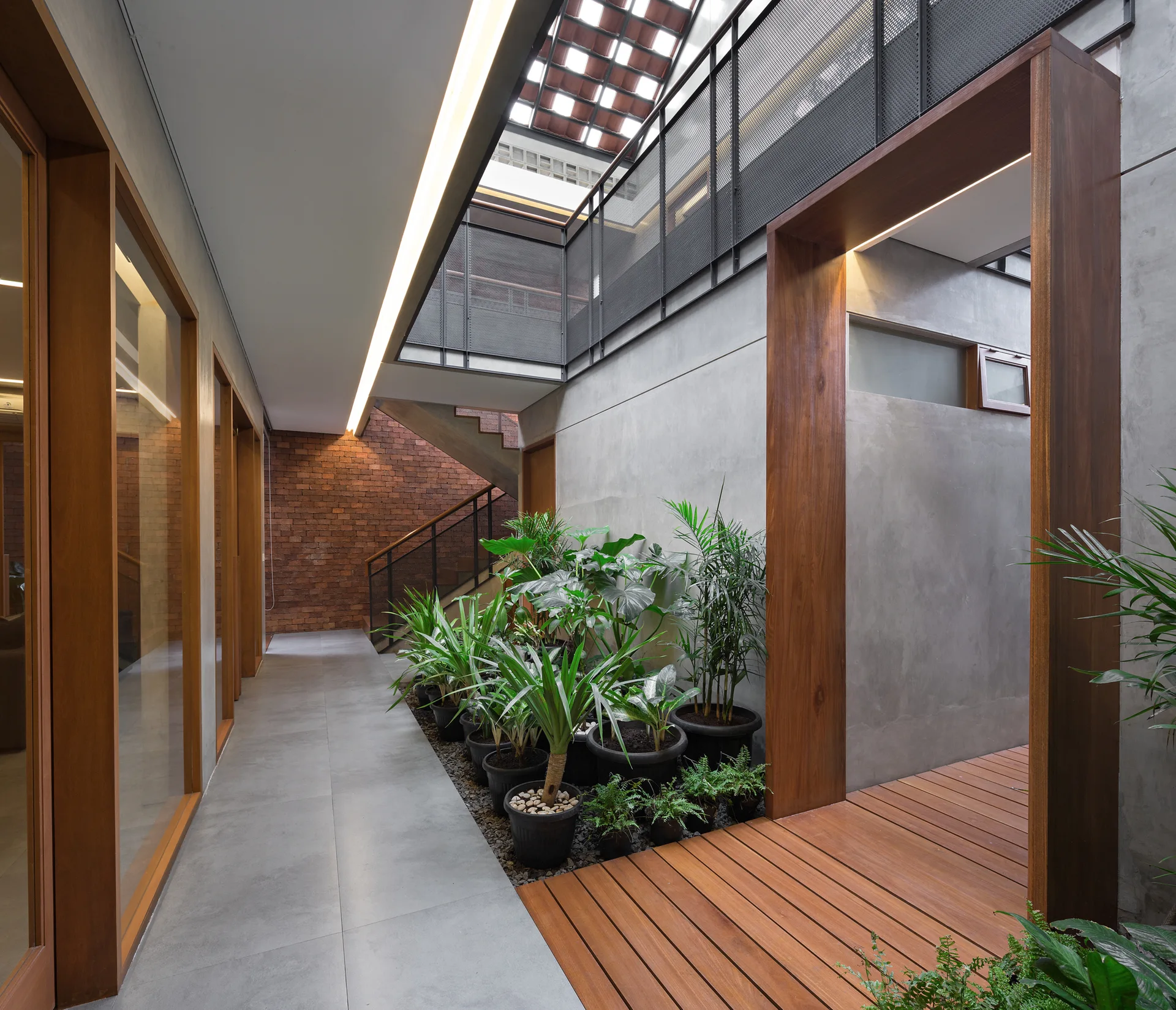 A modern hallway features exposed concrete walls, a tiled floor, an indoor gravel garden with potted plants, and a wooden walkway.
