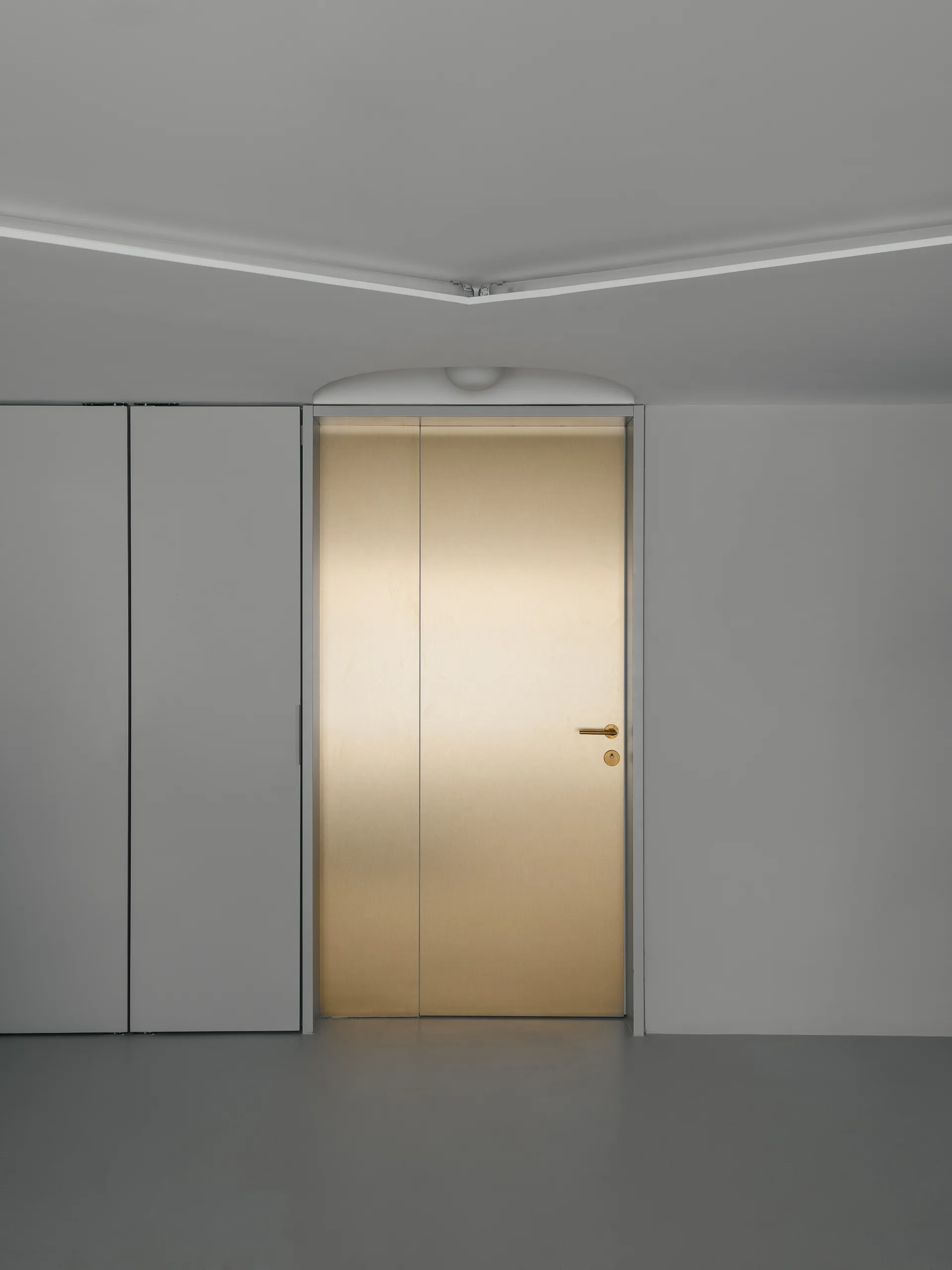 A flush-mounted metallic gold door with a brass handle is set between a smooth gray wall and integrated matte gray storage cabinets.