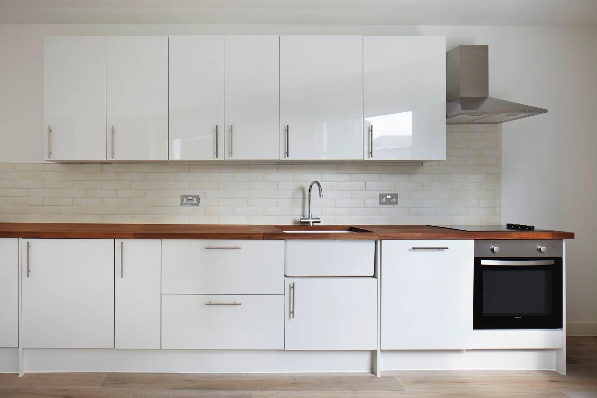 A modern kitchen with glossy white cabinetry, a warm wood countertop, a white farmhouse sink, and a subway tile backsplash.