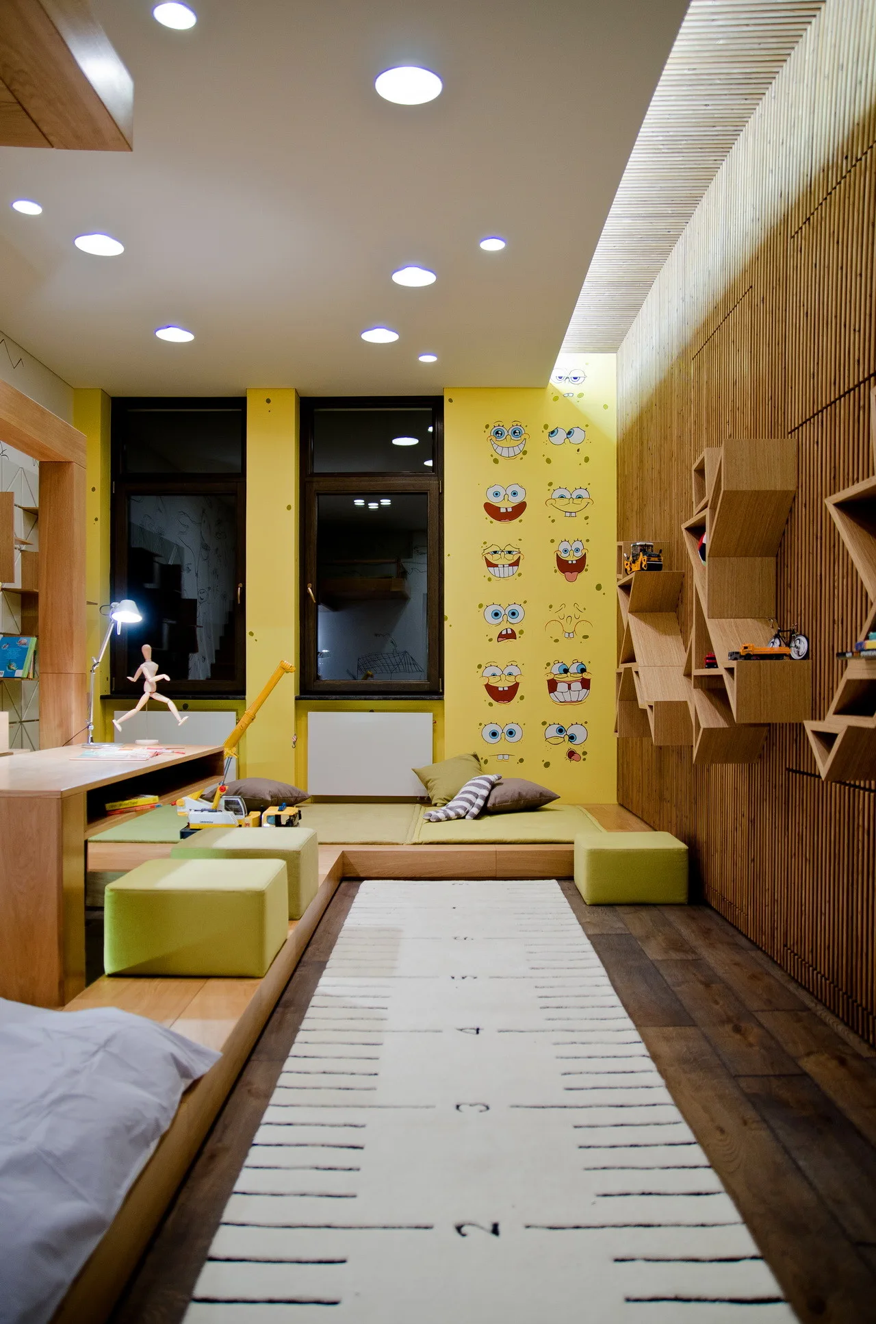 A kids bedroom features a yellow wall with cartoon decals, a vertical wood slat wall with geometric shelves, and a low platform seating area.