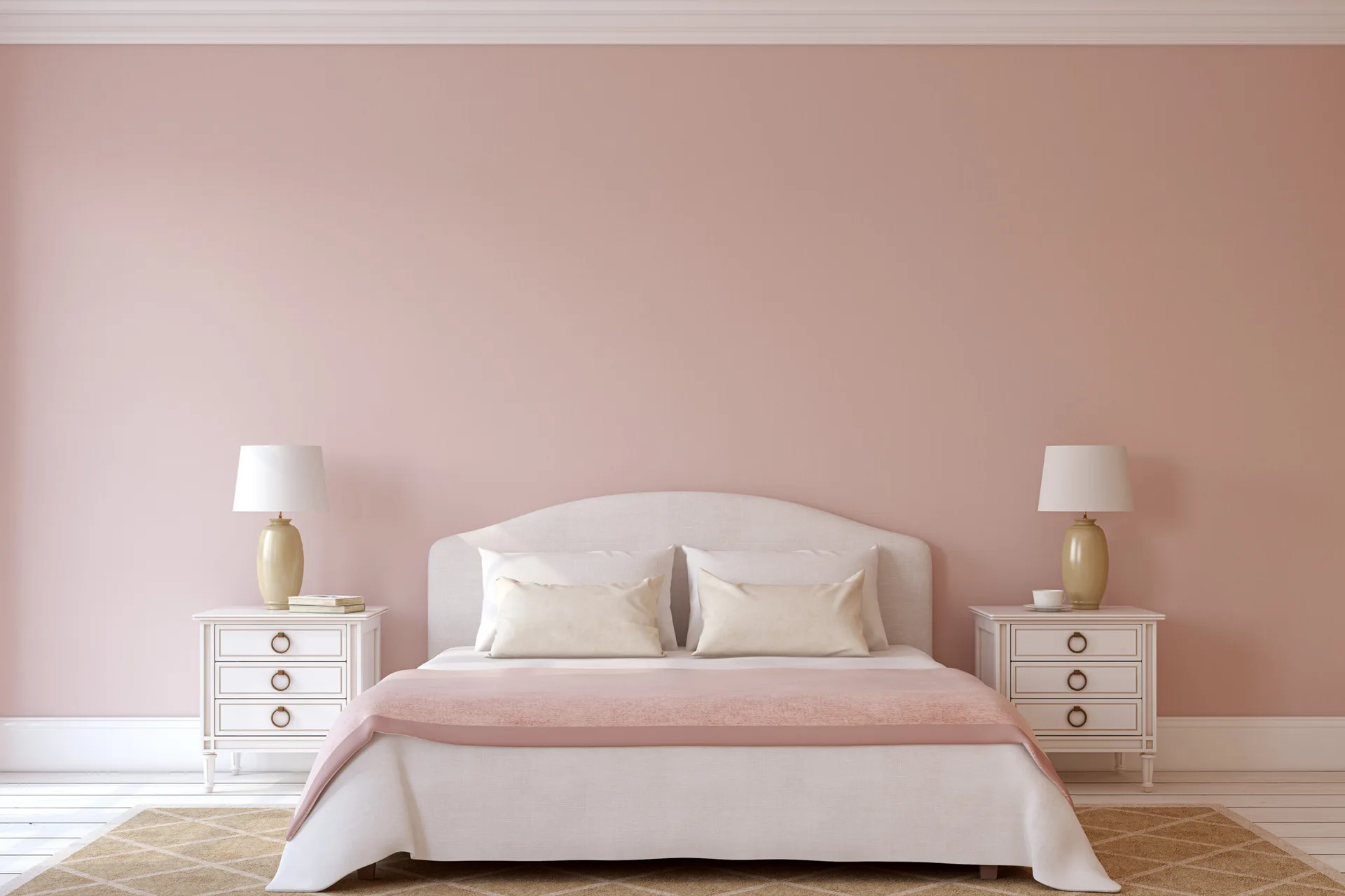 A symmetrically arranged bedroom features an upholstered white bed against a pink wall, flanked by two matching nightstands and gold lamps.