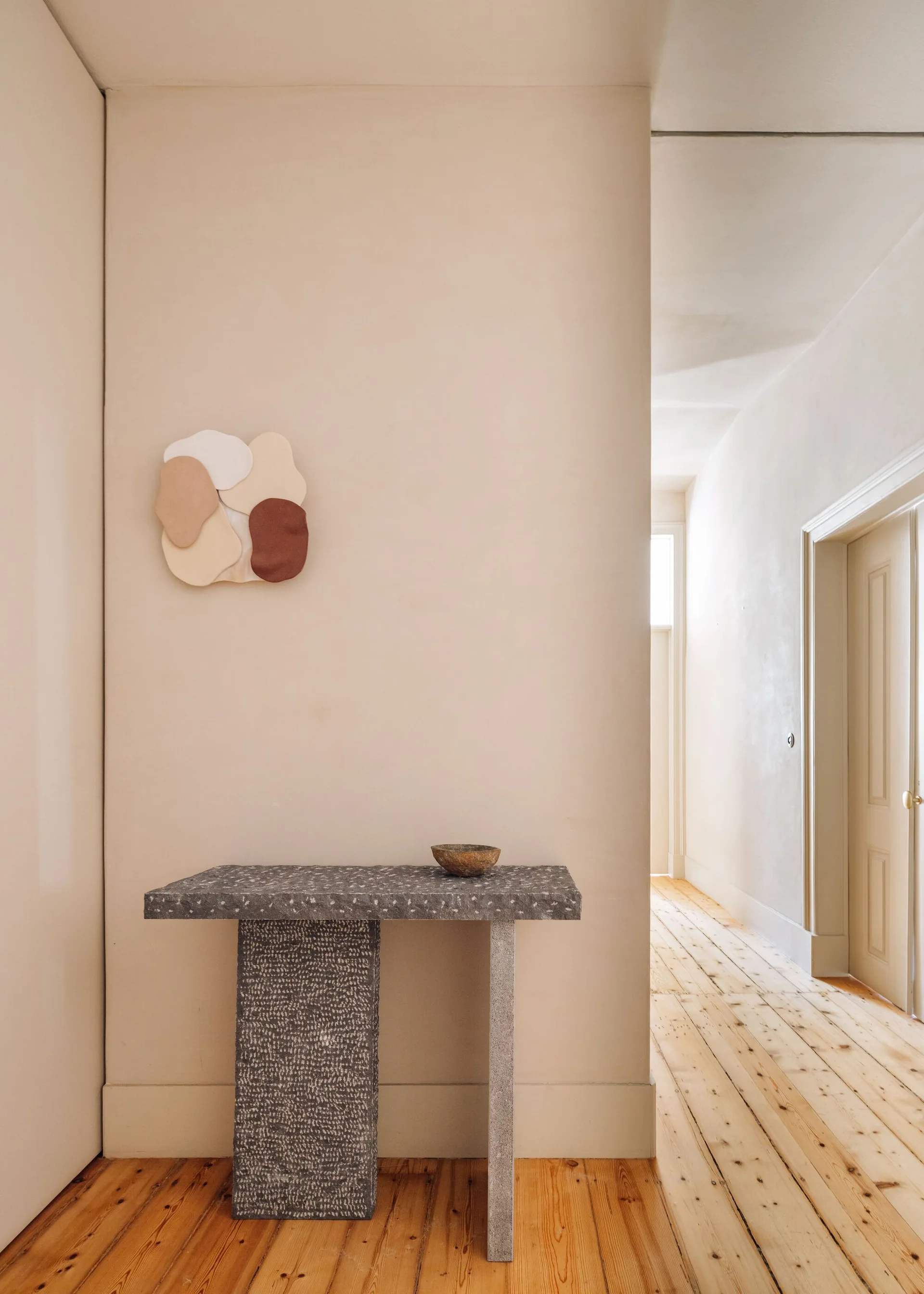 A speckled gray stone console table and organic-shaped wall art decorate a beige hallway with natural wood floors.