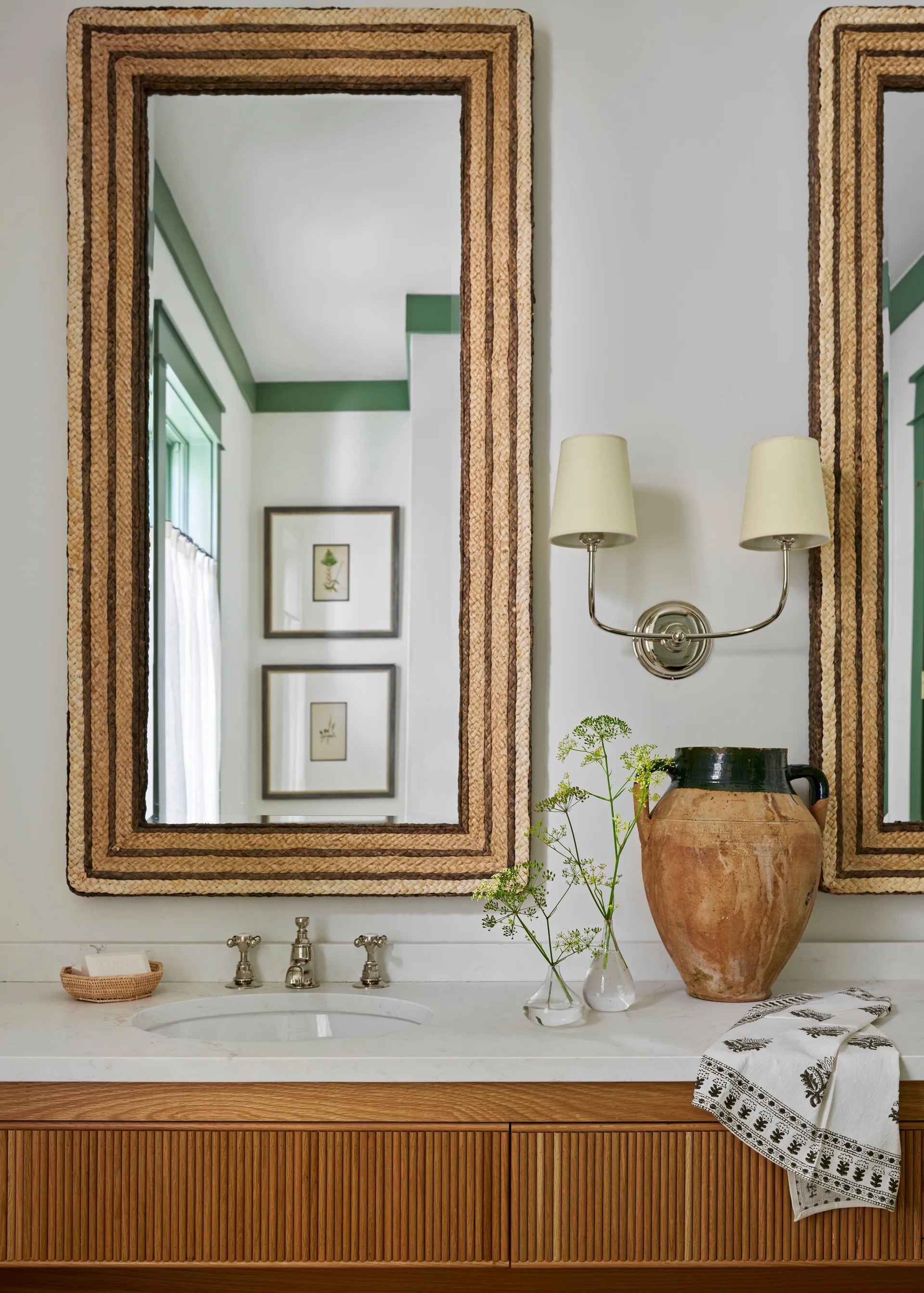 A bathroom vanity featuring a ribbed wooden cabinet, a white stone countertop, and a large mirror with a woven straw frame.