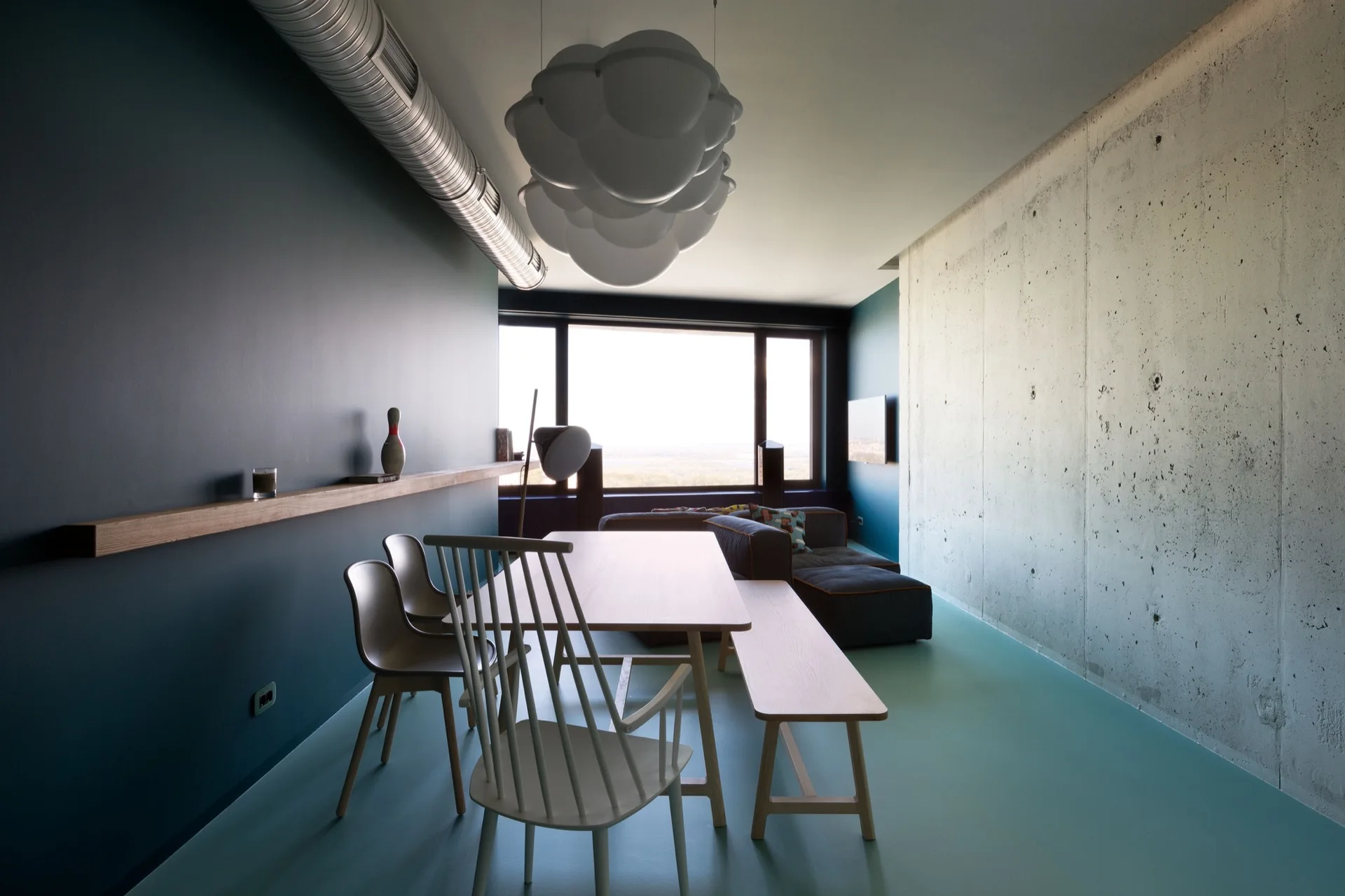 A modern dining room featuring a wooden table, mixed seating, a textured concrete wall, a dark blue wall, and a cloud-shaped pendant light.