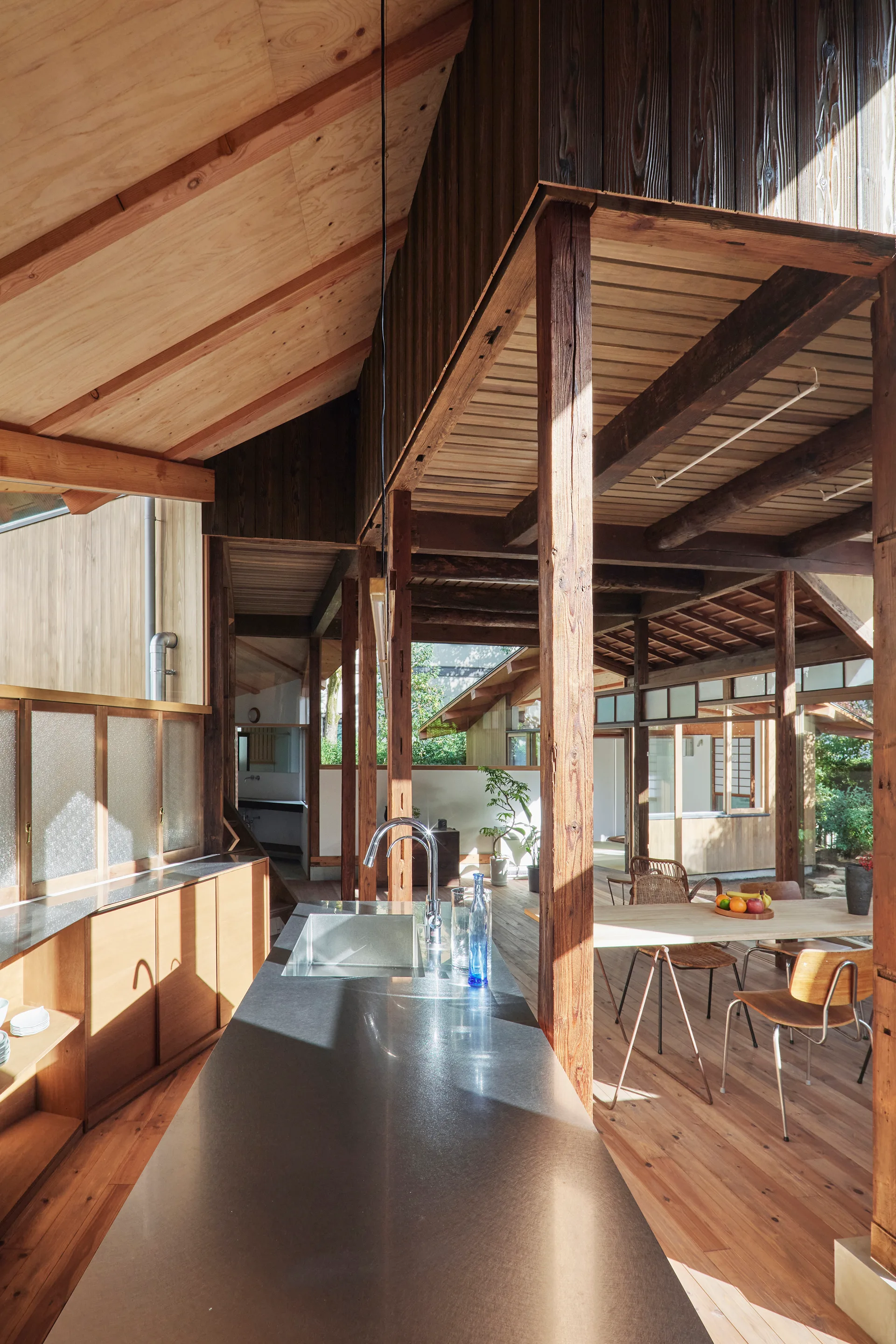 An open plan kitchen with a dark stone-top island under an exposed vaulted timber ceiling with supporting wooden columns.