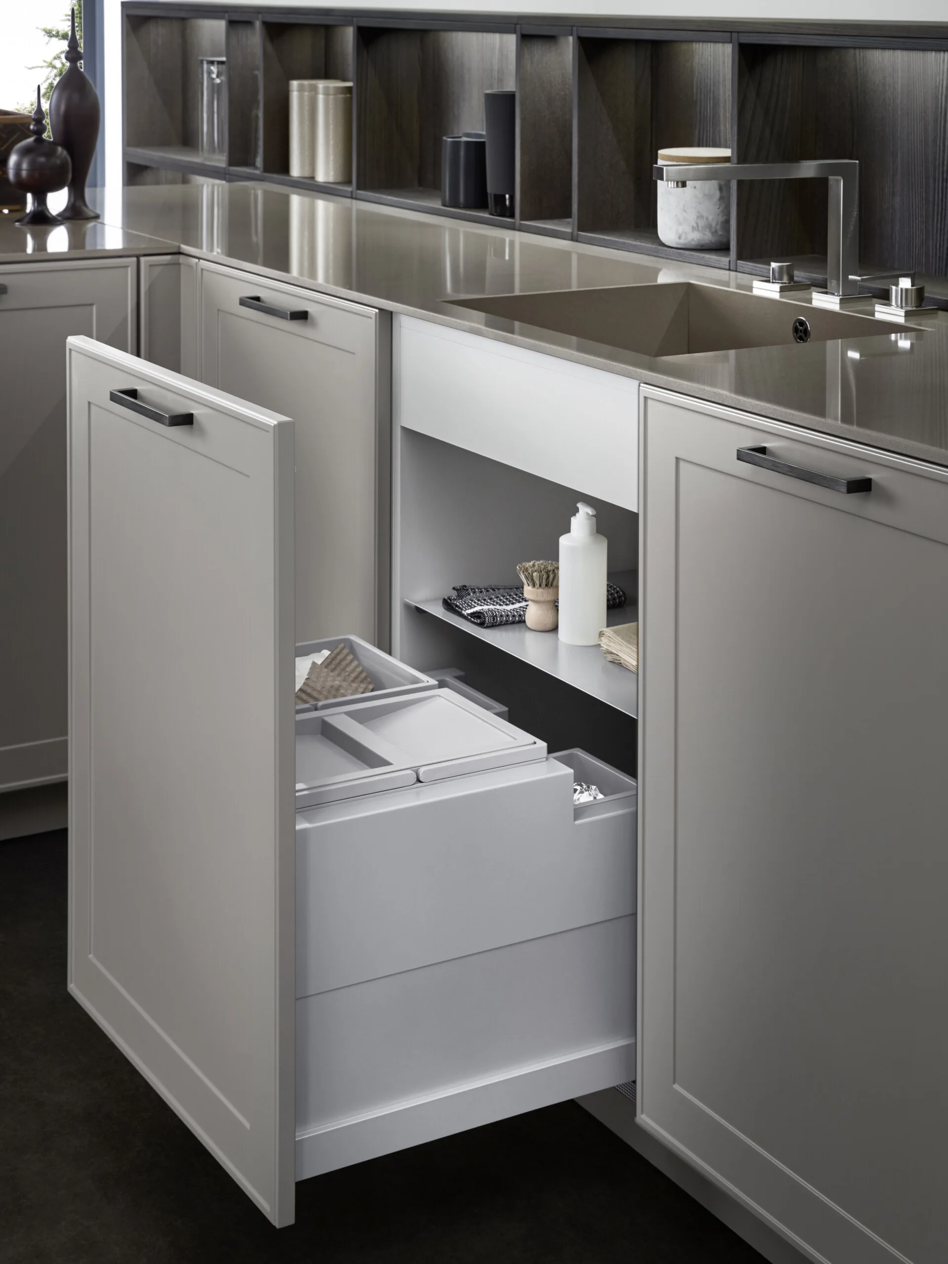 An open gray kitchen cabinet drawer with built-in recycling bins beneath a solid surface countertop.