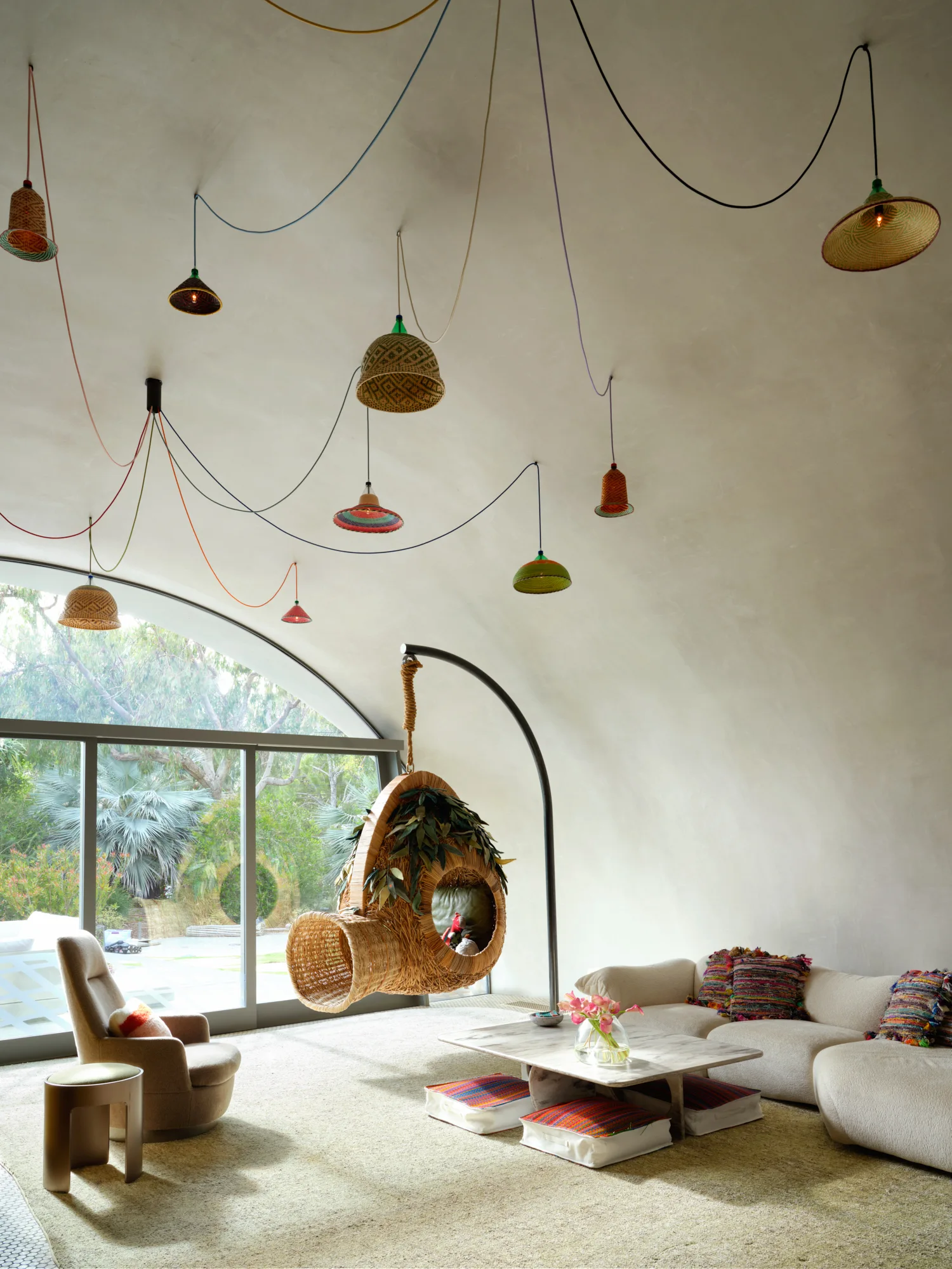 A living room featuring a curved plaster ceiling, cream sectional sofa, a hanging woven chair, and colorful swagged pendant lights.