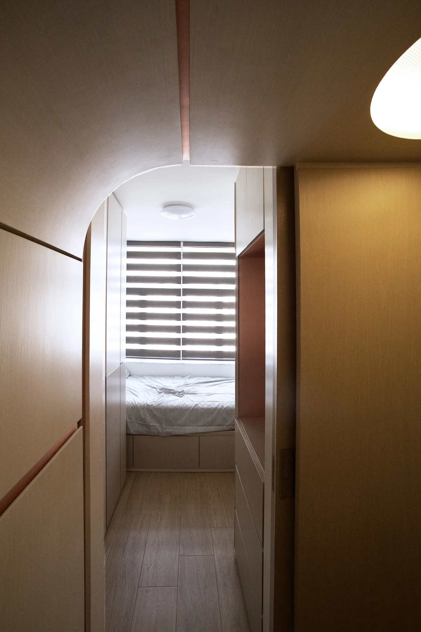 A small bedroom with a bed in an alcove is viewed through a wood-paneled archway flanked by built-in storage cabinets.