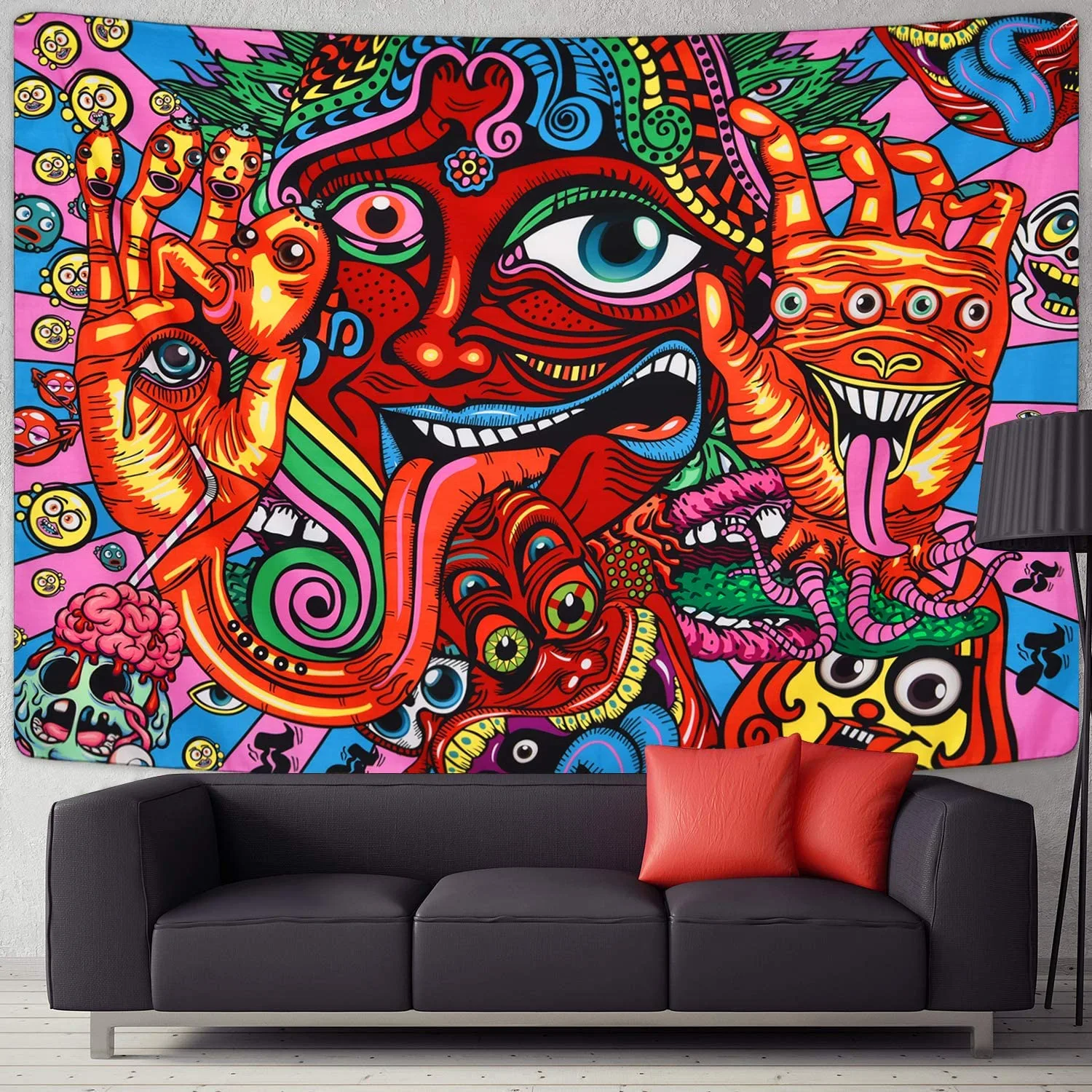 A black leather sofa with red throw pillows sits in front of a large, colorful psychedelic tapestry hanging on a white wall.