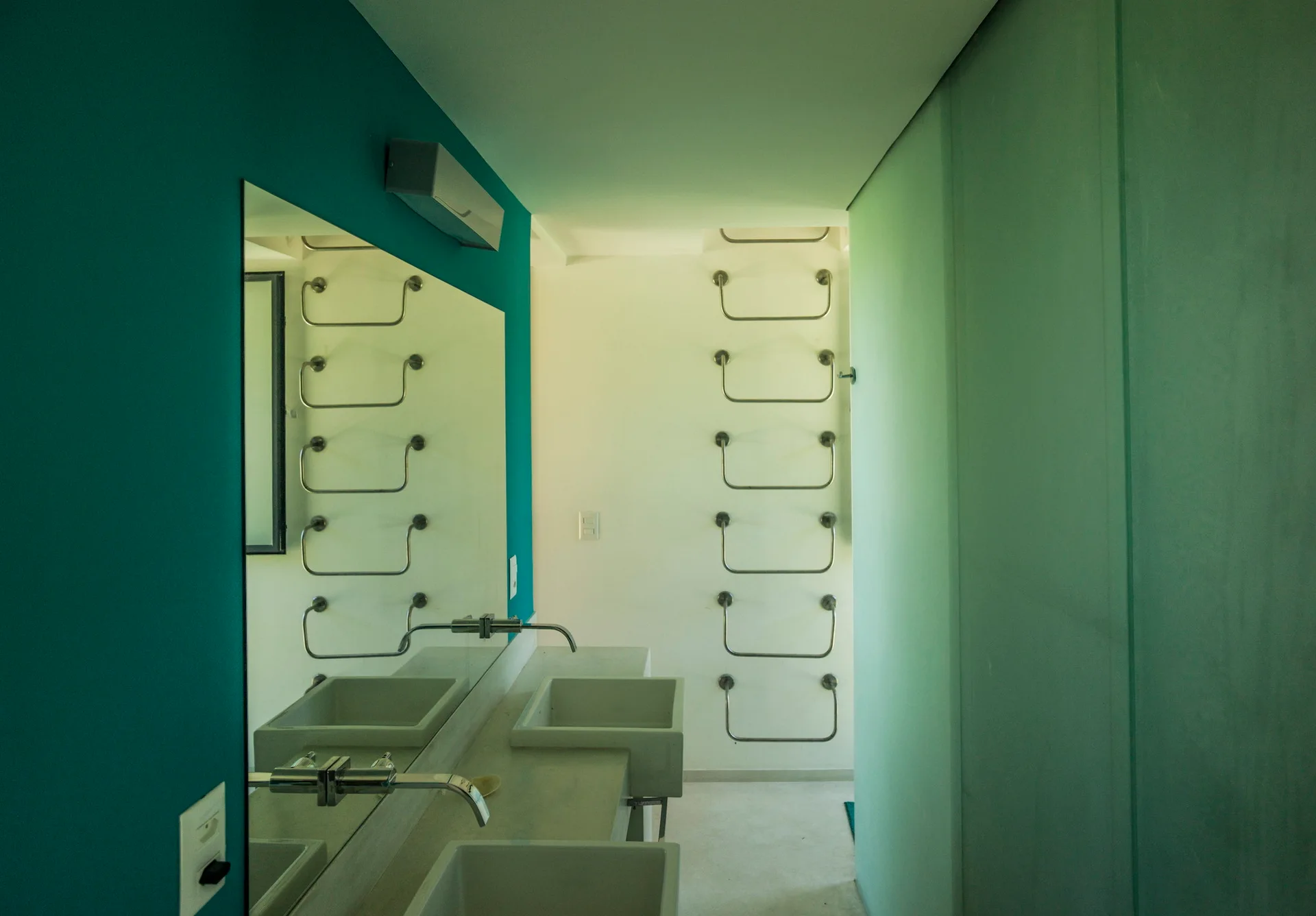A modern minimalist bathroom with a teal accent wall, double sinks with wall-mounted faucets, and metal towel rungs on a white background.