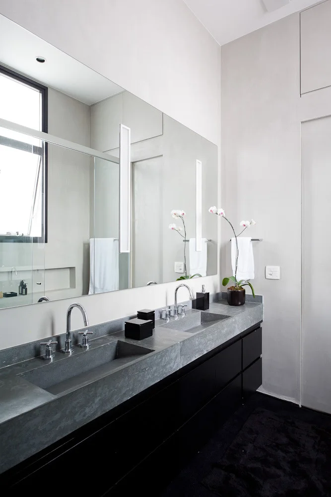 A modern bathroom features a double vanity with a grey concrete countertop, integrated sinks, black cabinetry, and a large mirror with vertical lights.