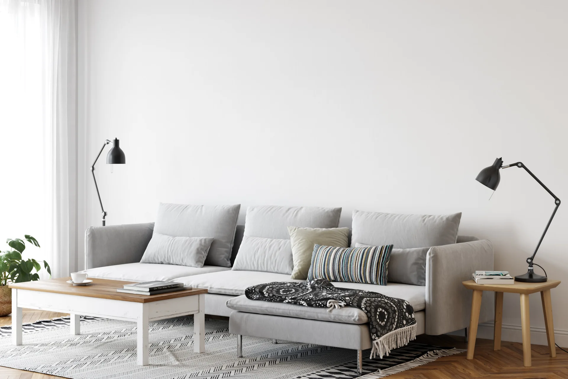 A light gray sectional sofa sits on a geometric patterned rug next to a white wooden coffee table and black metal lamps.