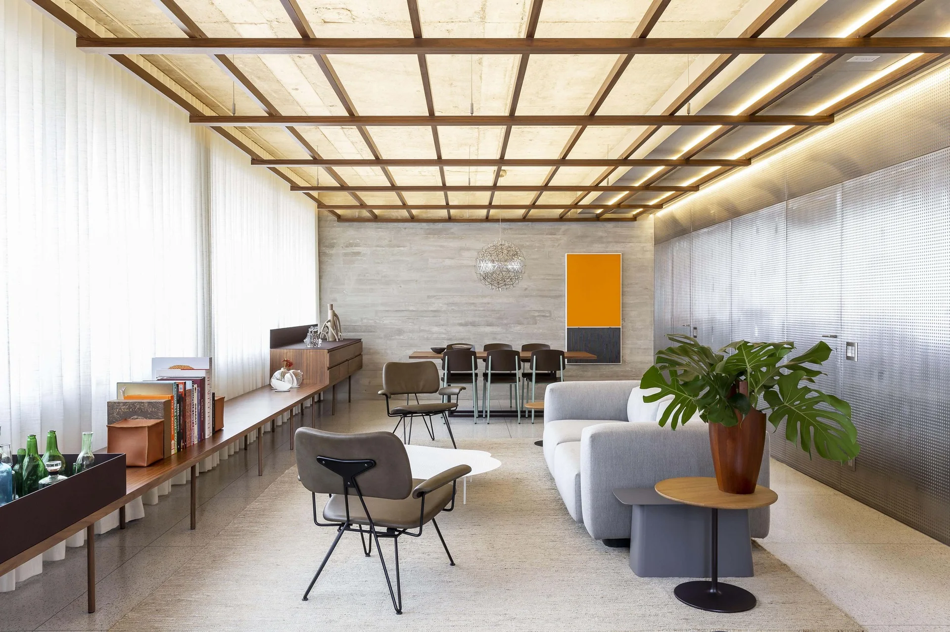 A modern open-plan living room featuring a grey sofa, brown leather chairs, a wooden grid ceiling, and a long low wood bench along a window wall.