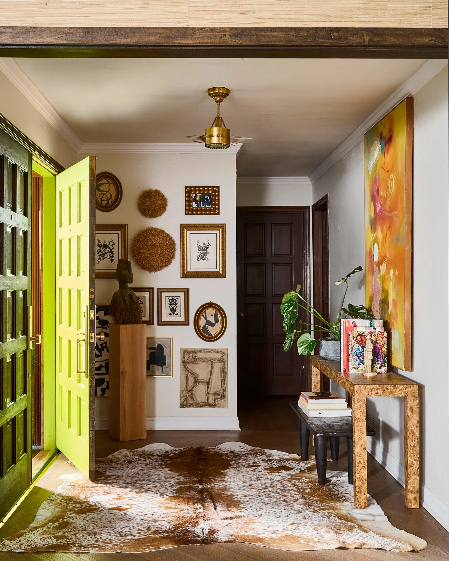 An eclectic entryway features a bright lime green front door, a gallery wall of framed art, a burl wood console table, and a cowhide rug.