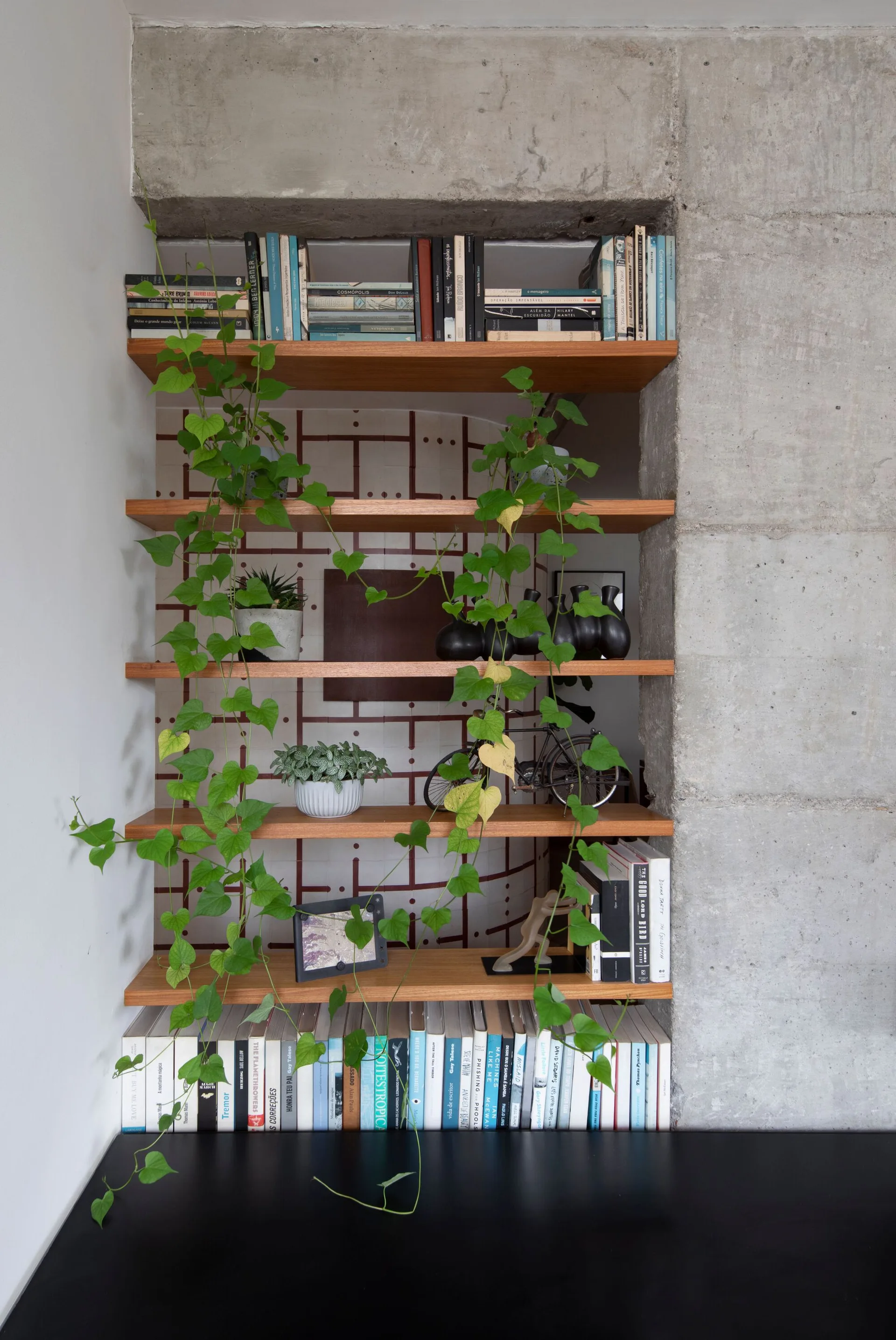 A recessed wooden shelving unit built into an exposed concrete wall and styled with books, plants, and small decorative items.