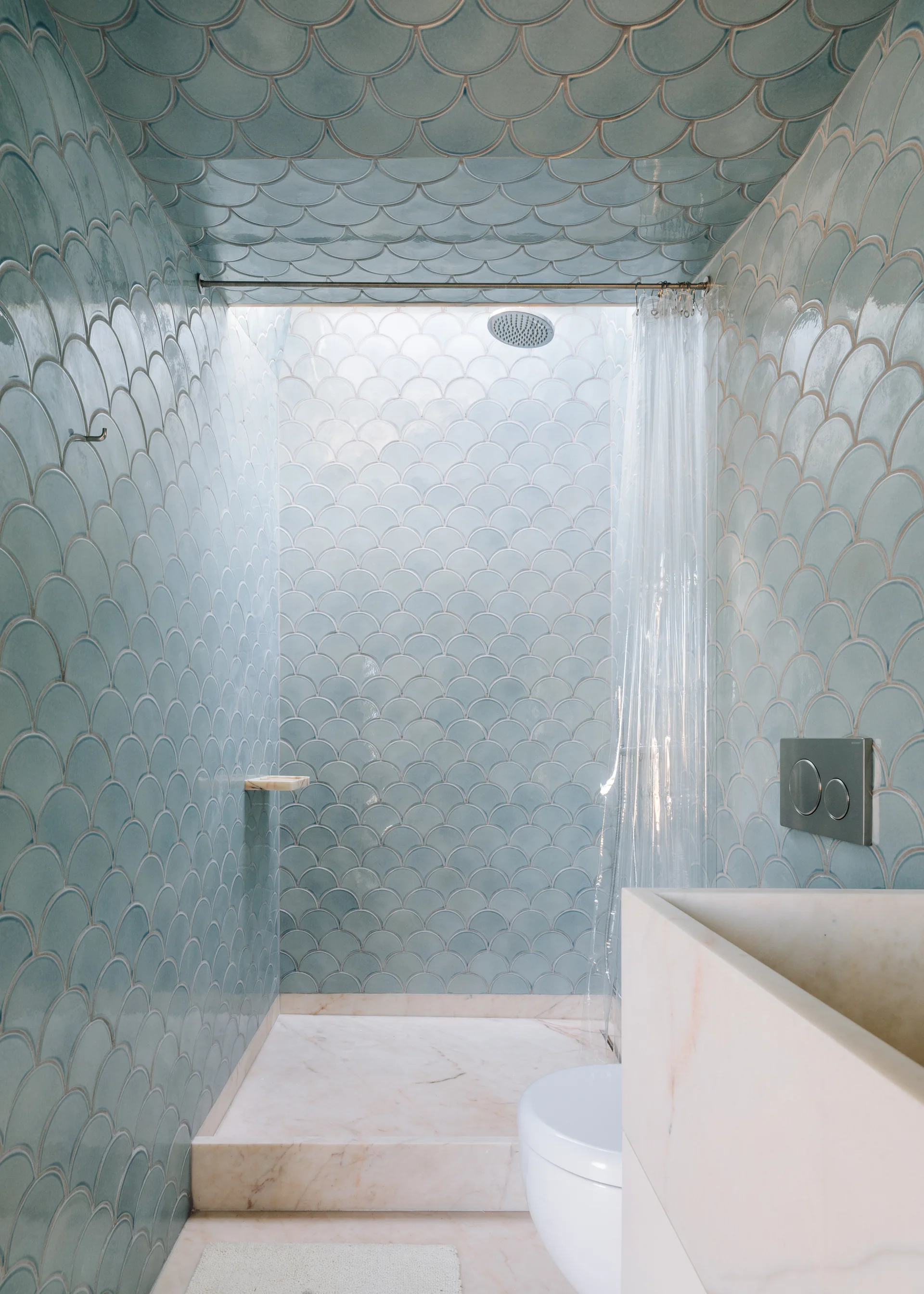 A bathroom featuring light blue scalloped tiles on the walls and ceiling, a marble floor, and a marble vanity unit.