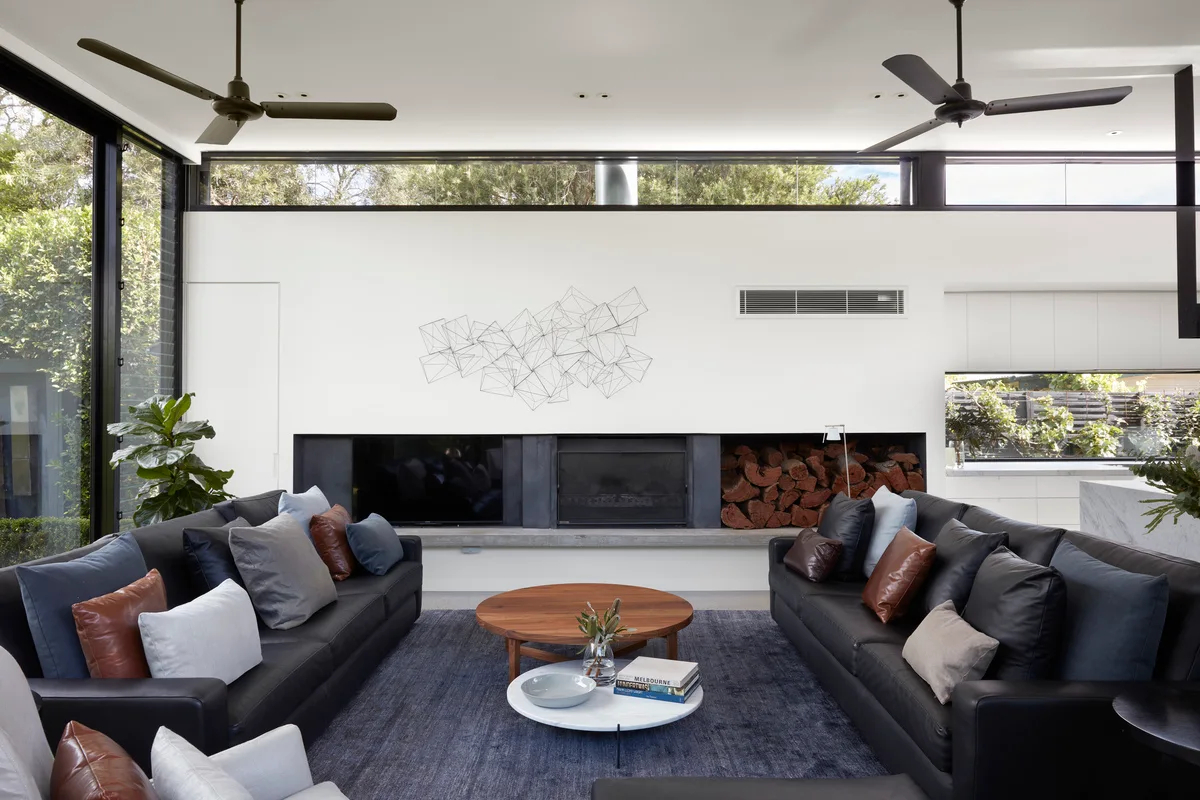 A modern living room featuring two black leather sofas facing a low linear fireplace with a built-in wood storage niche and a white wall above.