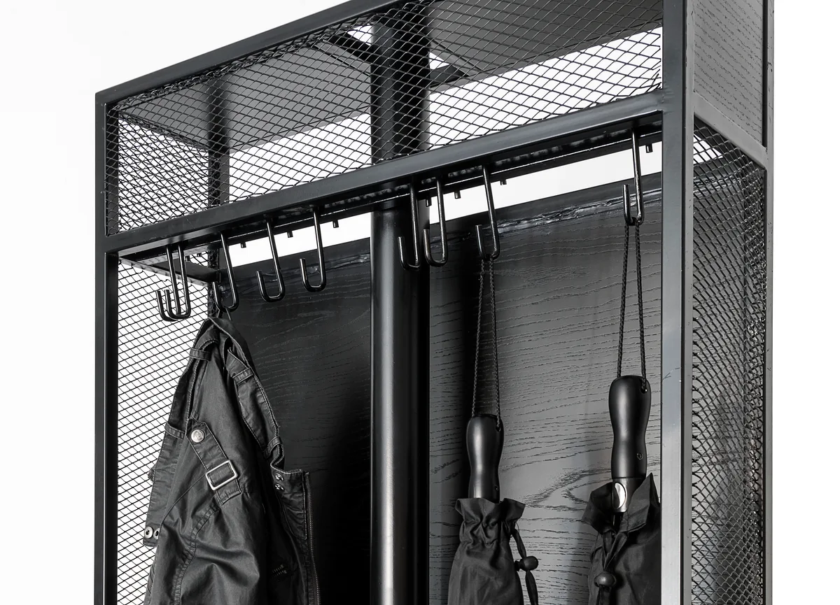 A close-up of a matte black metal coat rack featuring wire mesh side panels, top shelving, and several hanging hooks with a jacket and umbrellas.