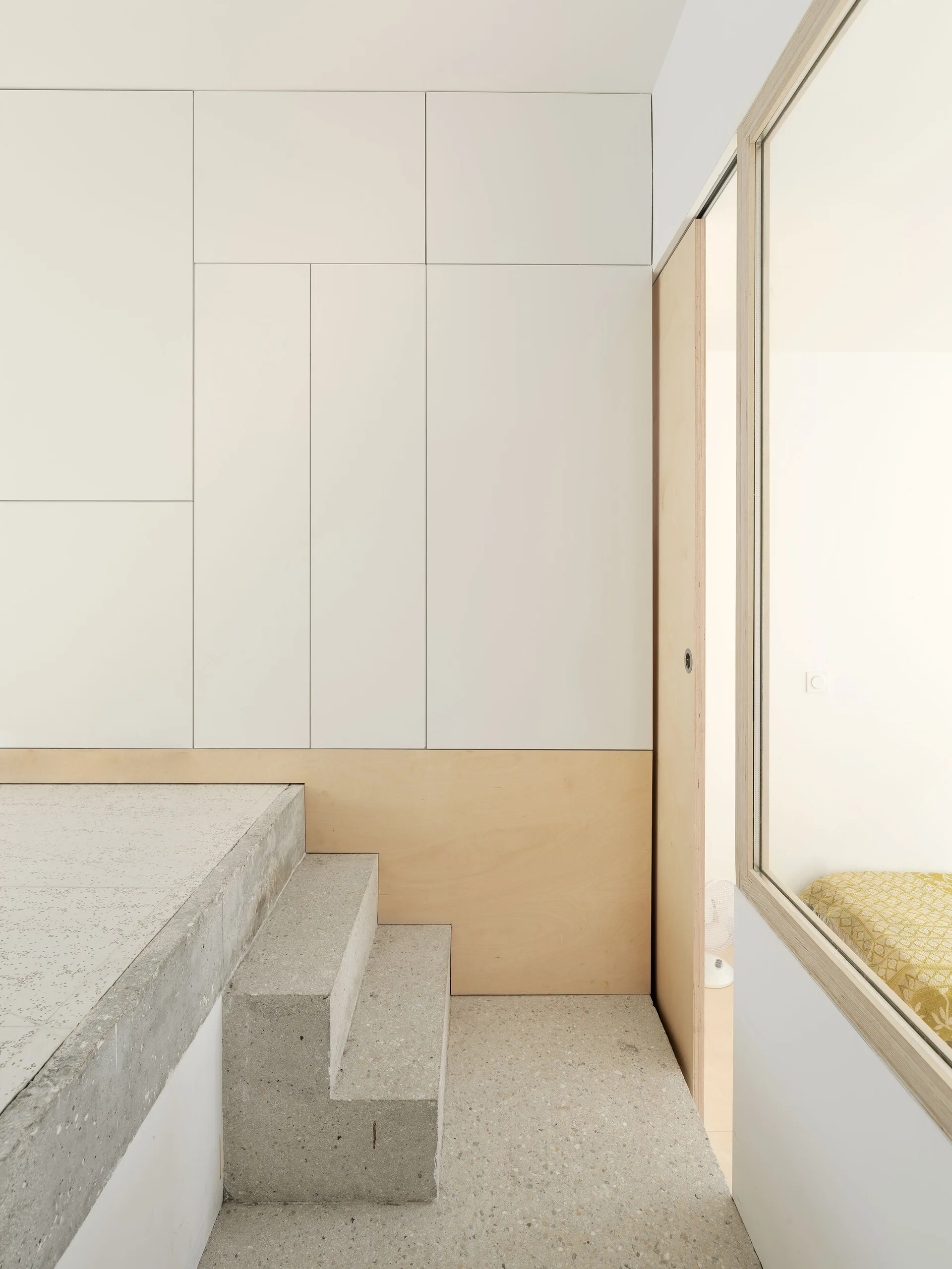 Minimalist interior view featuring speckled terrazzo steps leading to a landing next to white cabinetry and a light wood sliding door.