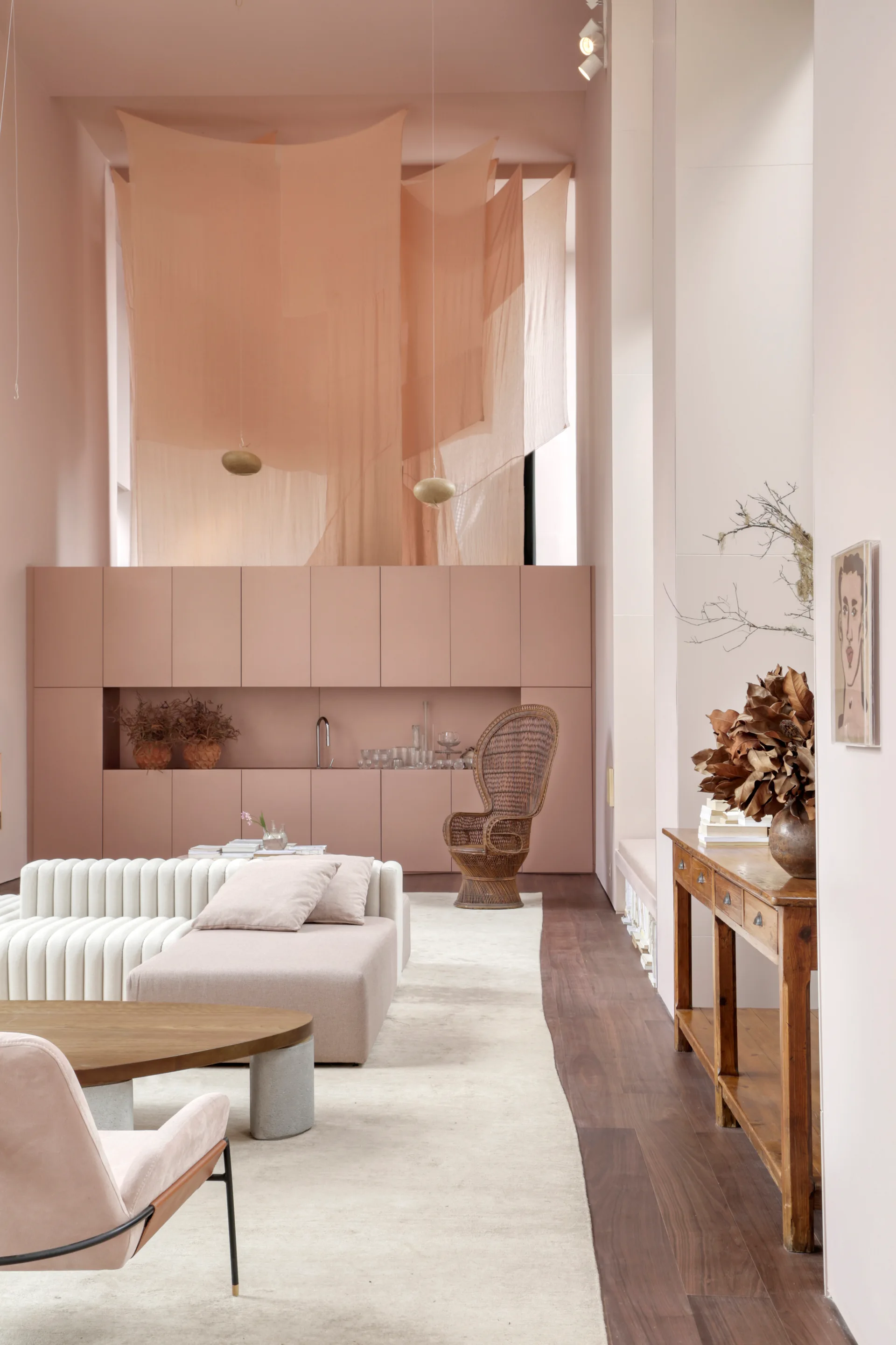 A pink living room features a white modular sofa, a built-in mauve cabinet wall, and sheer fabric panels hanging from the high ceiling.