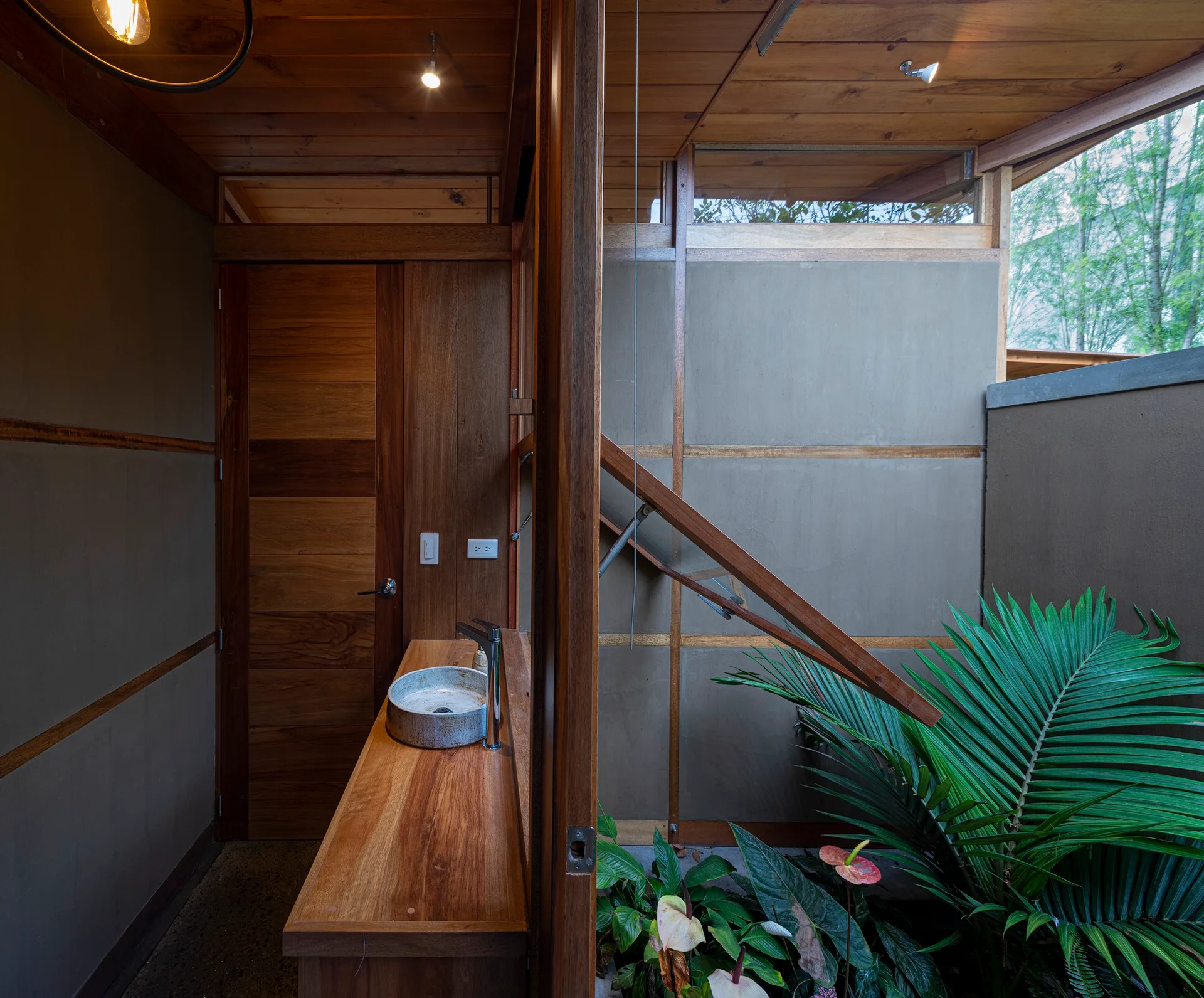 An organic modern bathroom featuring a natural wood vanity, a stone vessel sink, and large tropical plants under a wood ceiling.