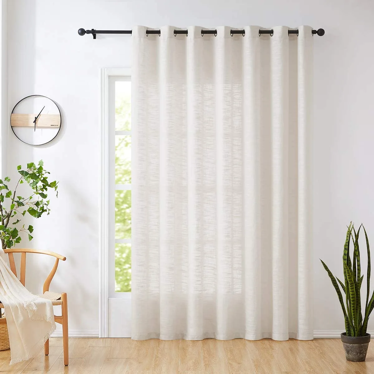 A textured white sheer curtain with dark metal grommets hangs from a black rod in a bright room with light wood floors.