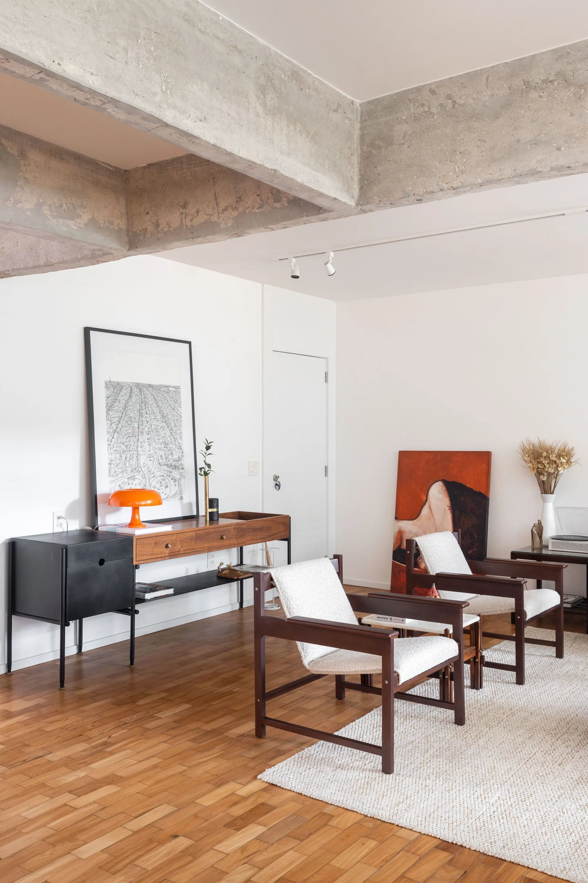Two mid-century wooden armchairs and a wood console table sit on a white textured rug beneath an exposed concrete ceiling beam.