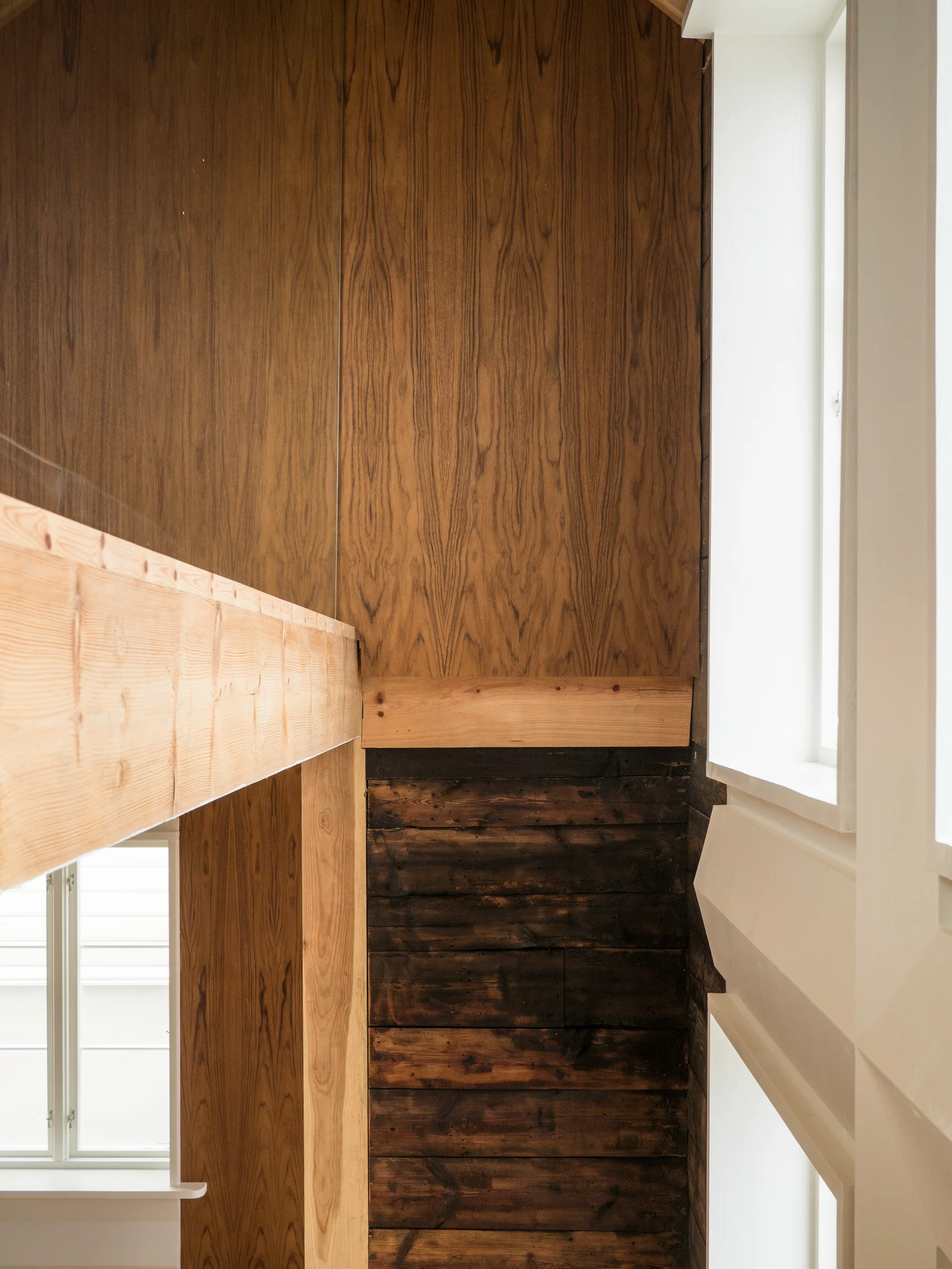 Architectural detail of a mezzanine structure showing contrasting light wood panels, a dark horizontal wood wall, and white window trim.