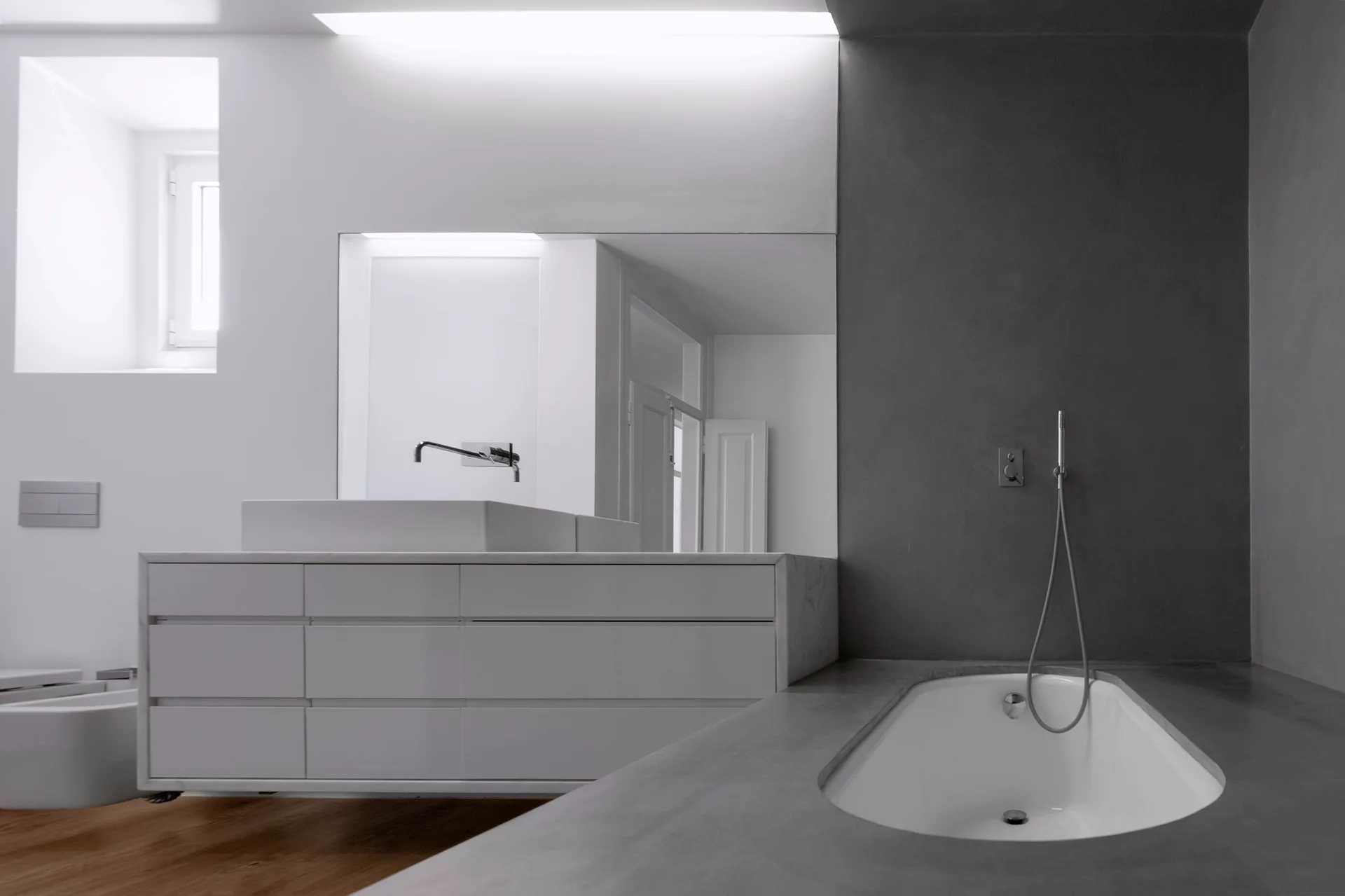 A minimalist bathroom features a floating white vanity with a rectangular sink alongside a built-in bathtub encased in grey concrete.