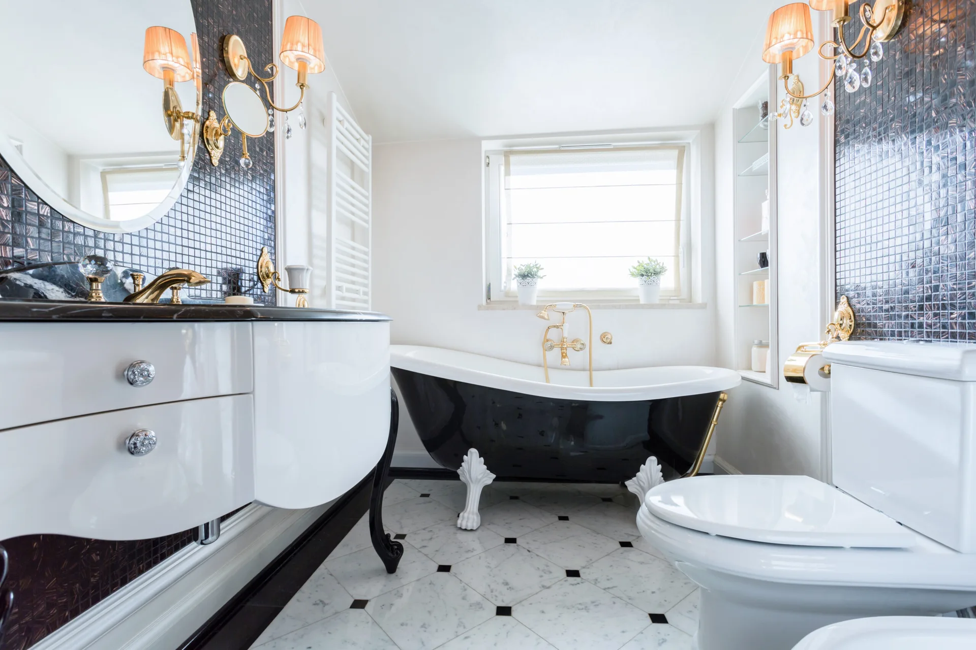 A monochrome bathroom features a black and white clawfoot bathtub, a curved white vanity with gold hardware, and dark mosaic wall tiles.