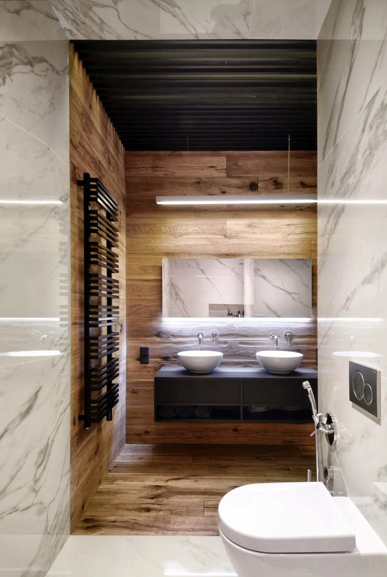 A modern bathroom features a floating black vanity with dual white vessel sinks, wood paneled walls, white marble tile, and a black slatted ceiling.