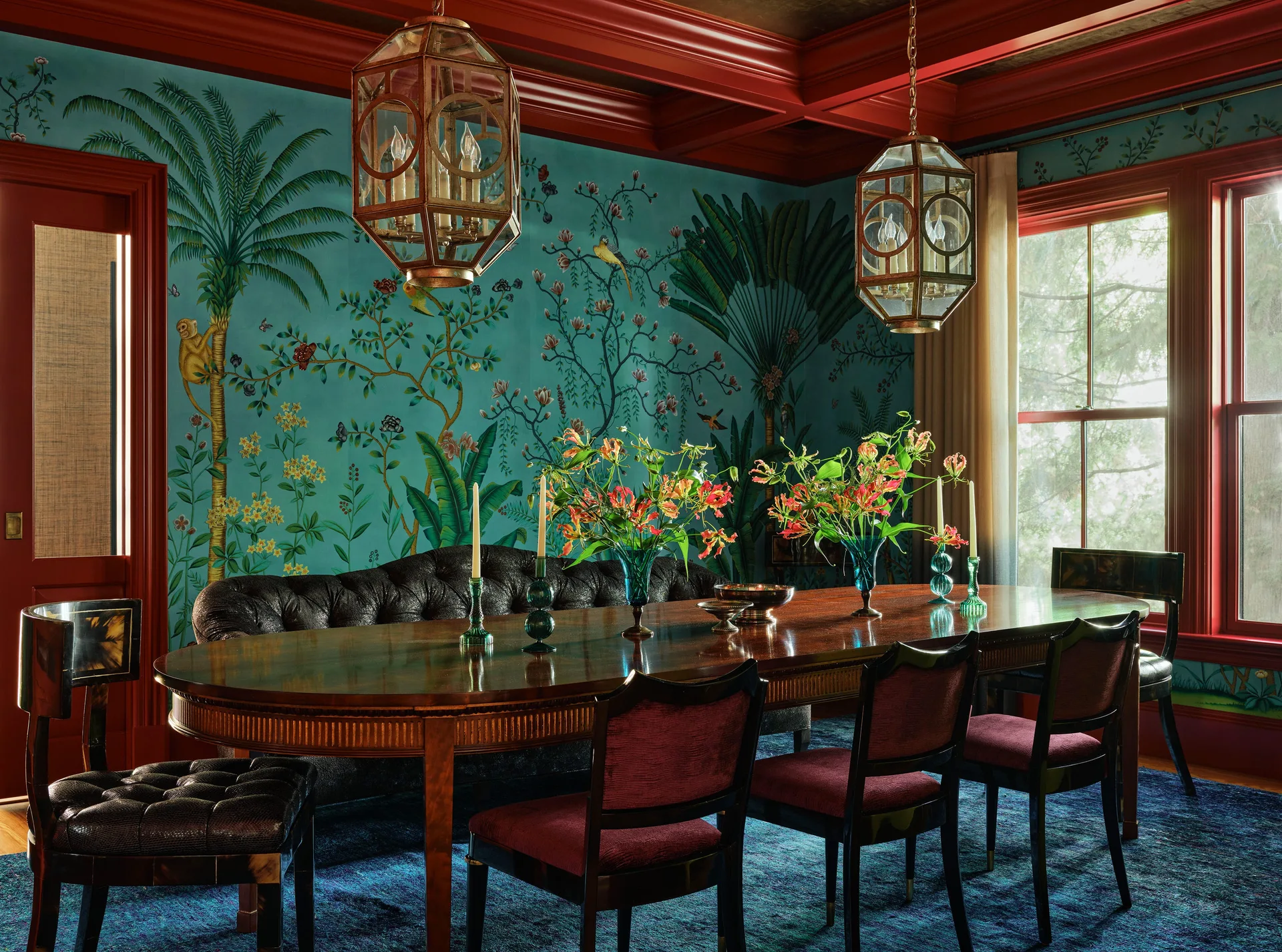 A formal dining room features a dark wood table with upholstered chairs, red coffered ceilings, brass hanging lanterns, and teal botanical wallpaper.