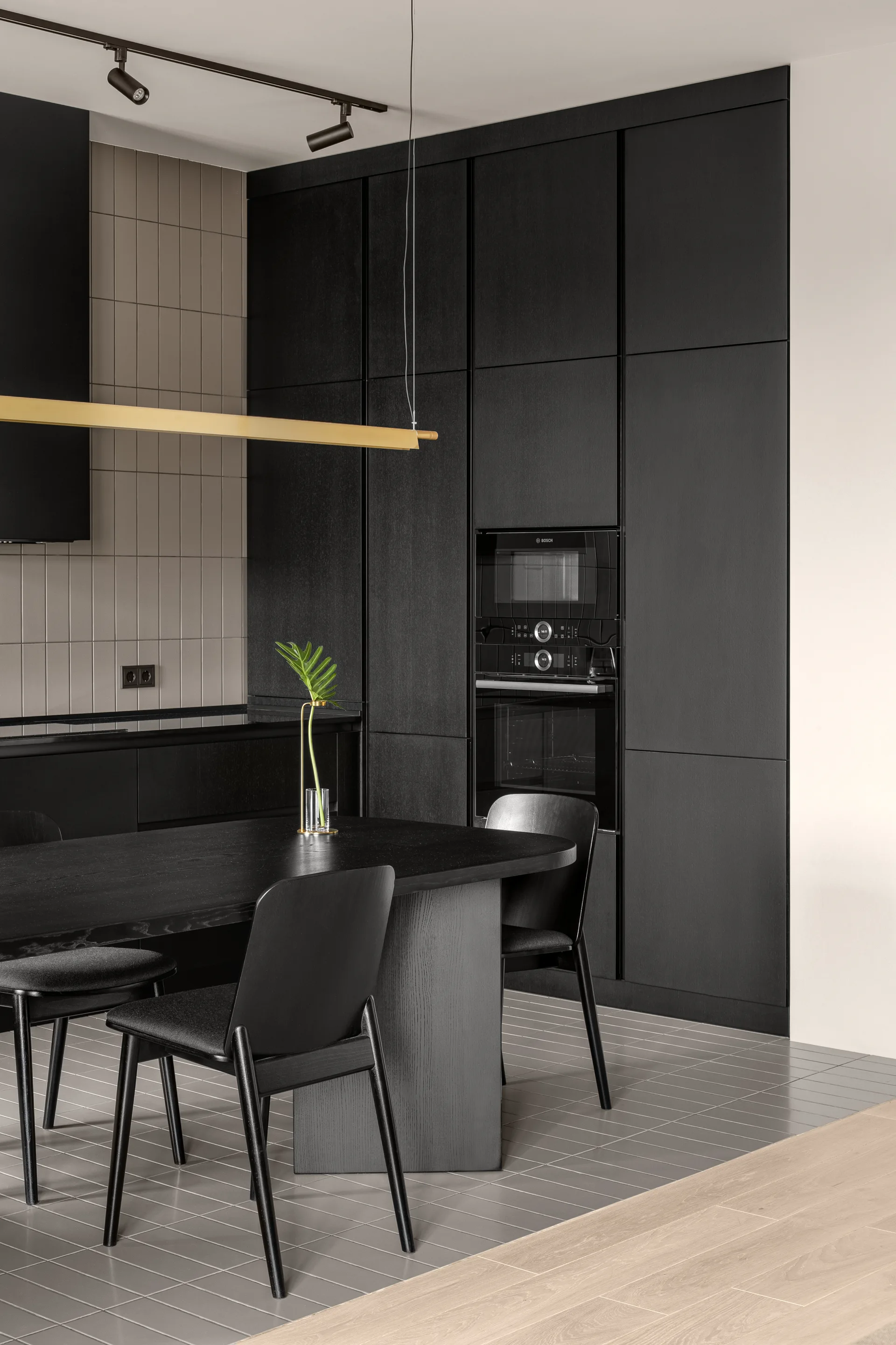 A modern kitchen featuring matte black floor-to-ceiling cabinets, an integrated black oven, a grey tiled floor, and a black dining table with chairs.