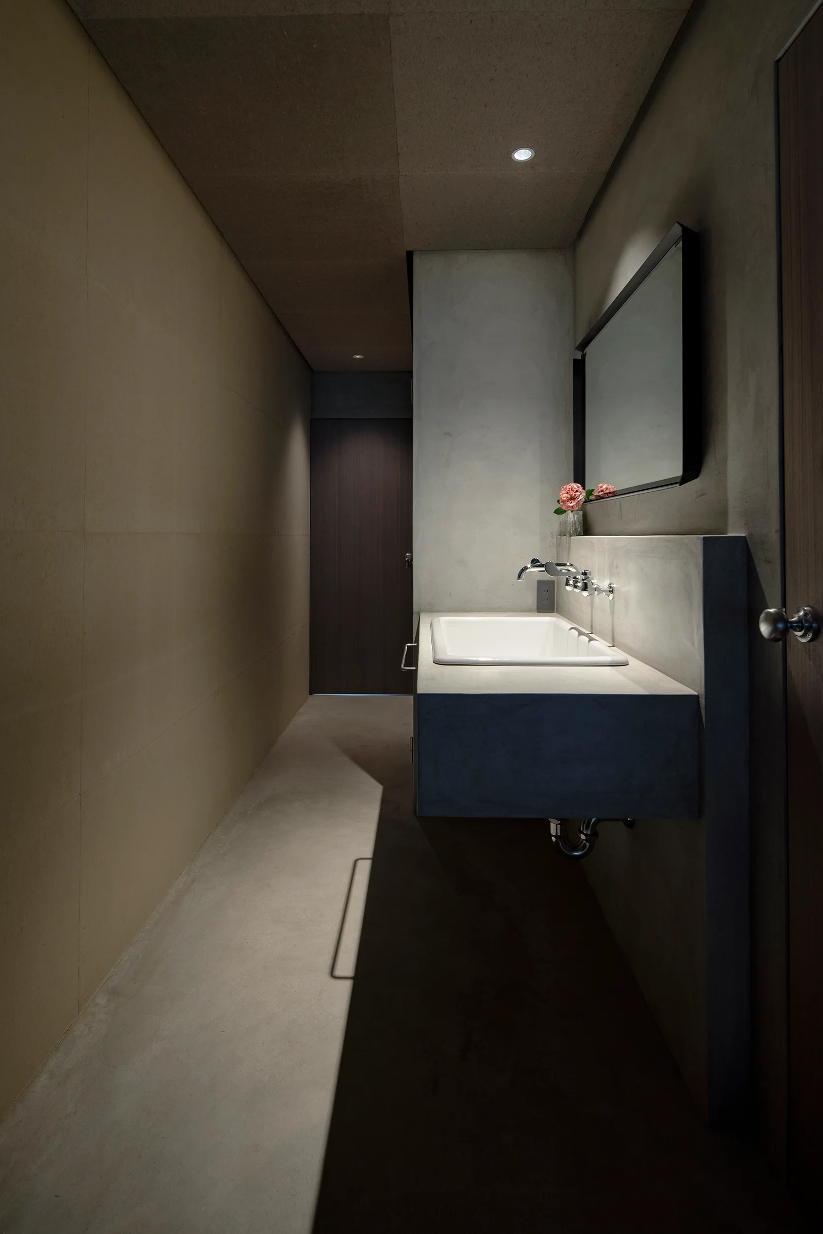 A minimalist bathroom features a gray concrete floating vanity with a white sink, a black-framed mirror, and smooth plaster walls.