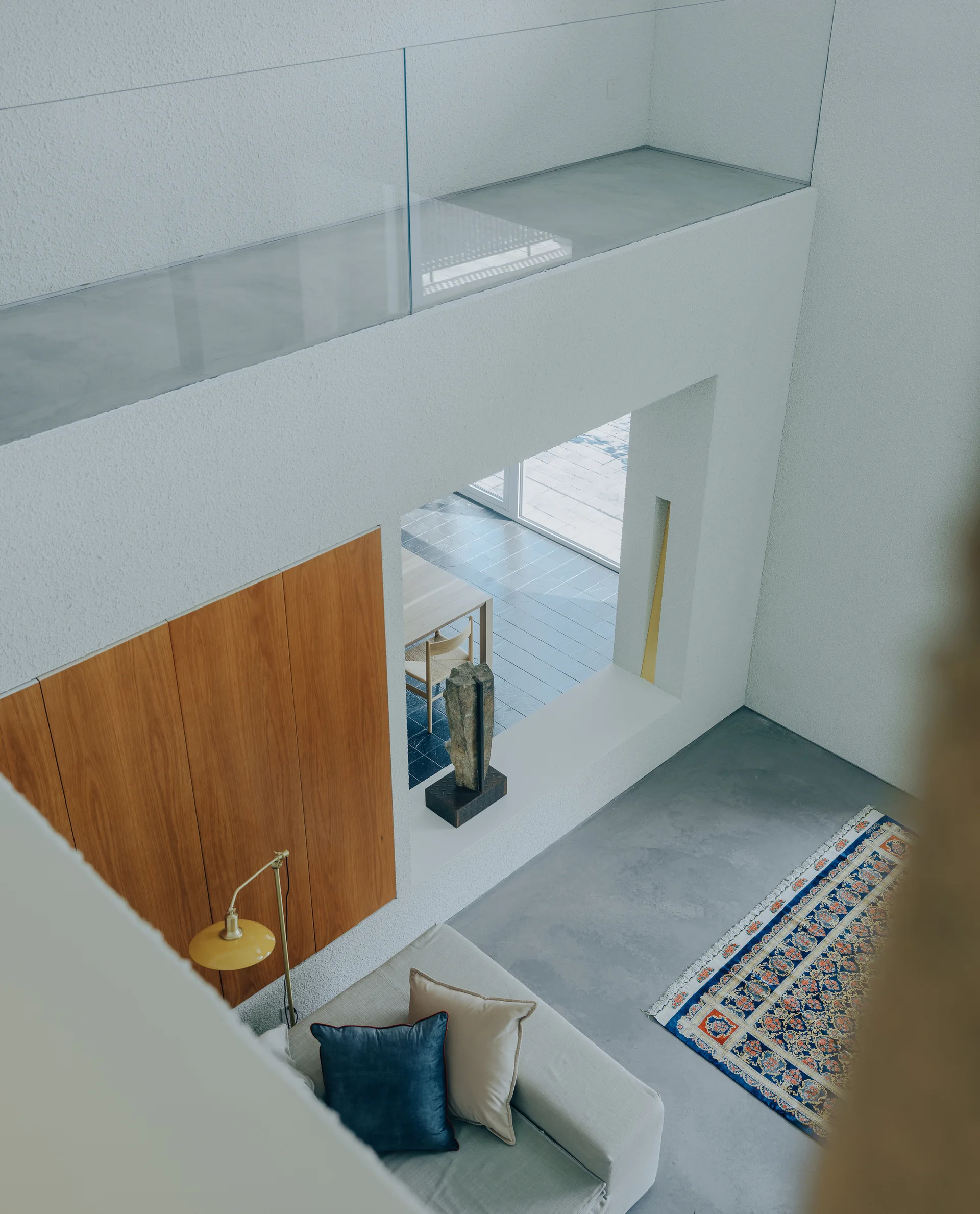 Looking down into a modern living room featuring a concrete floor, a beige sofa with blue pillows, a patterned rug, and a built-in wood cabinet.